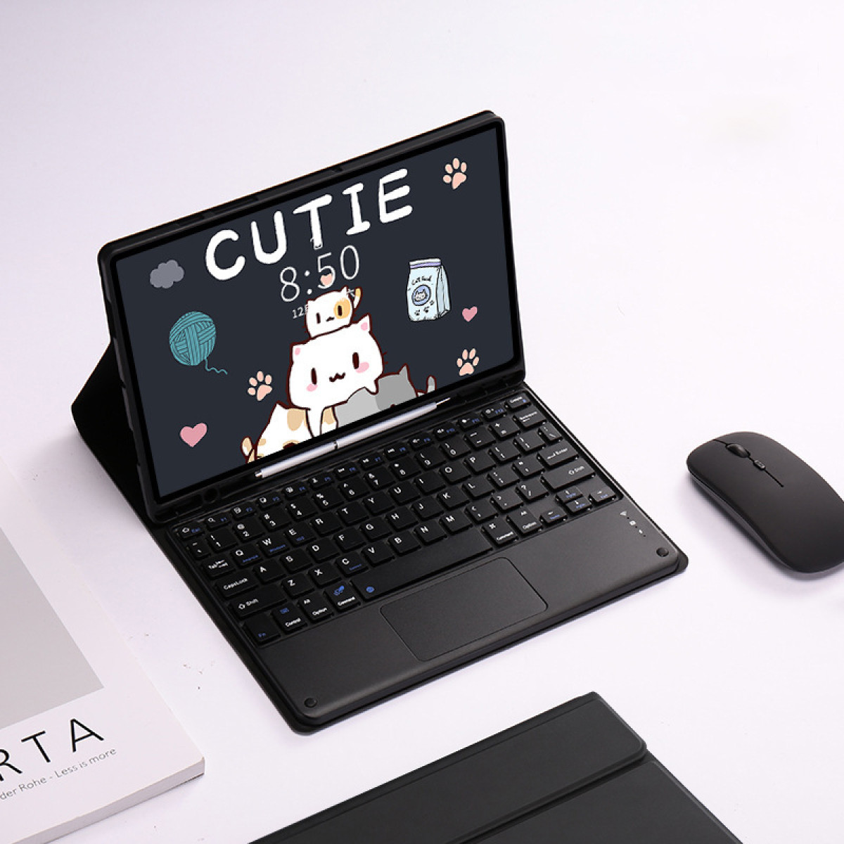 Czarny tablet z klawiaturą, myszką i ekranem z motywem kota. Obok leży książka.