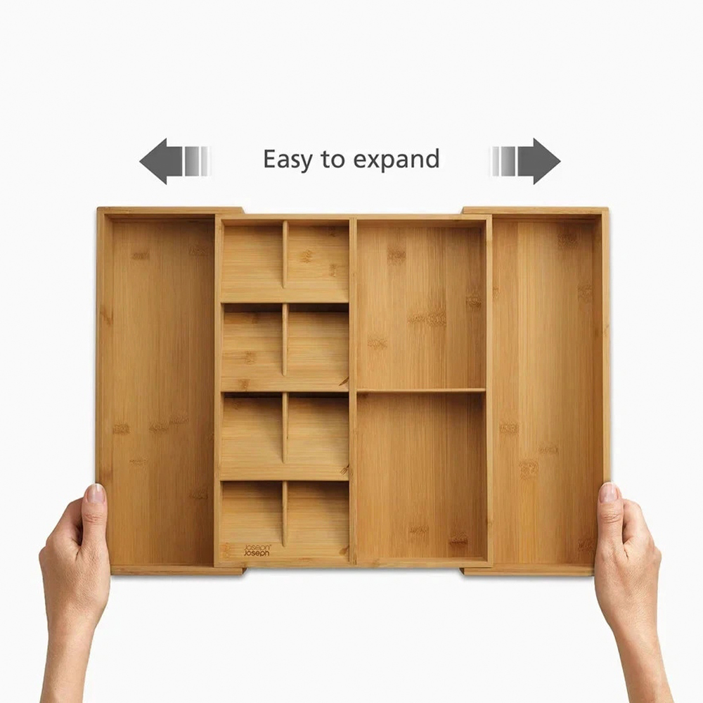 Se muestra un organizador de cajones de madera expandible. Tiene varios compartimentos. Las manos sostienen los lados, con flechas que indican expansión.