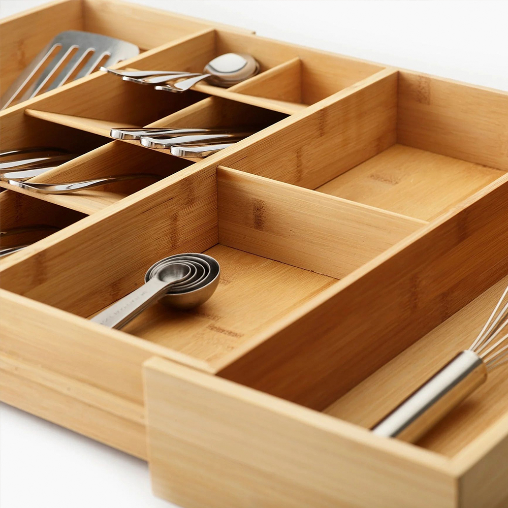 Un organizador de cubiertos de madera con compartimentos que contienen cucharas, tenedores, una espátula, cucharas medidoras y un batidor.