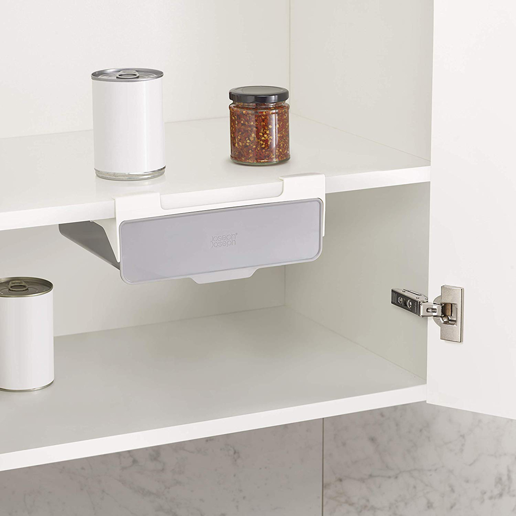 Dentro de un armario blanco hay dos latas, un frasco con contenido y un cajón gris colgando de un estante.