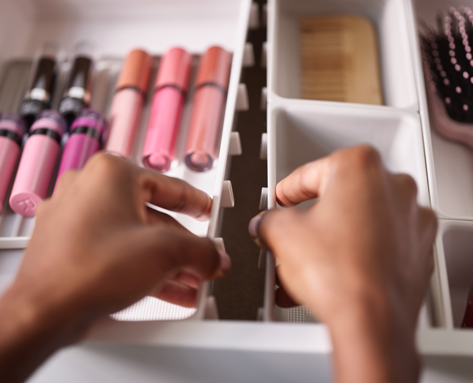Manos abriendo un organizador de maquillaje blanco. Se ven labiales y un peine. Las manos son de piel morena.
