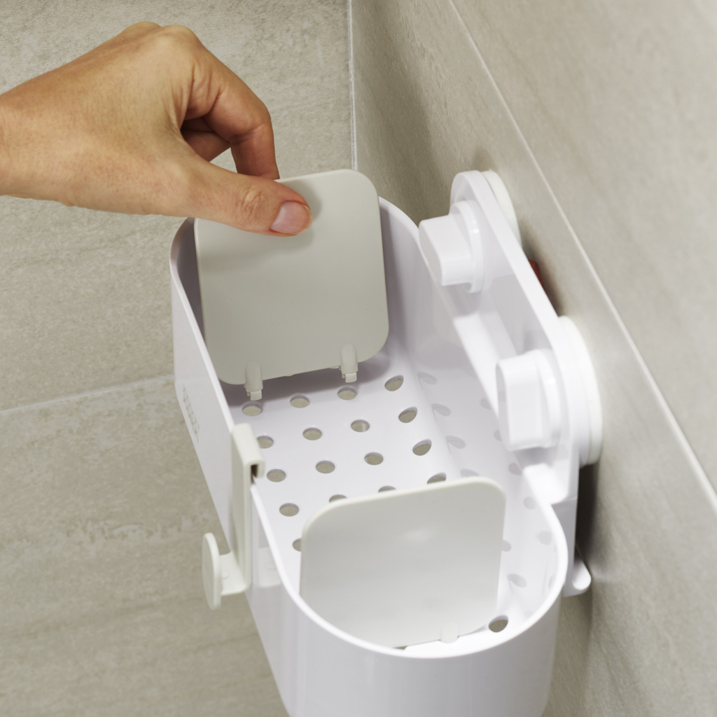 Una mano coloca un panel gris en un organizador de baño de plástico blanco montado en una pared de azulejos.