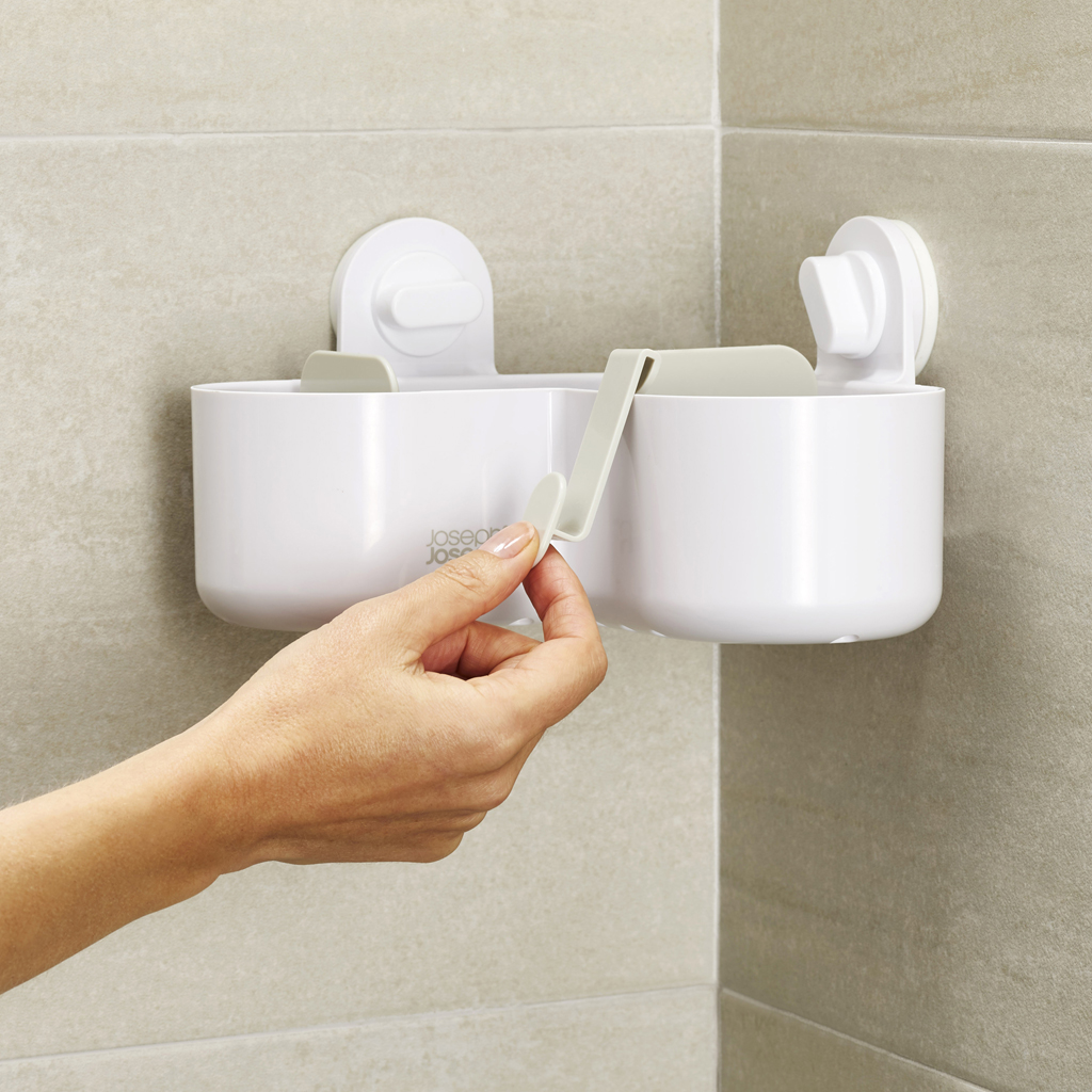 Una mano tira de un gancho gris claro en un organizador de baño blanco fijado a una pared alicatada.