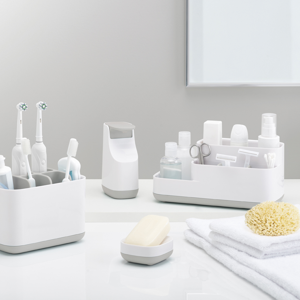 Badezimmer mit weißen und grauen Organisatoren, die Toilettenartikel, elektrische Zahnbürsten, Seife und Handtücher enthalten. Ein gelber Schwamm ist ebenfalls vorhanden.