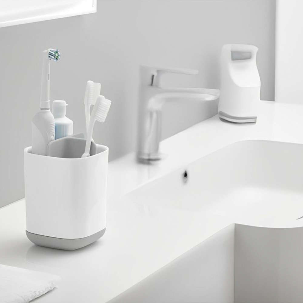 Weißer Badzähler mit Waschbecken und Wasserhahn. Ein Zahnbürstenhalter hat Zahnbürsten und Zahnpasta. Eine weiße elektrische Zahnbürste.