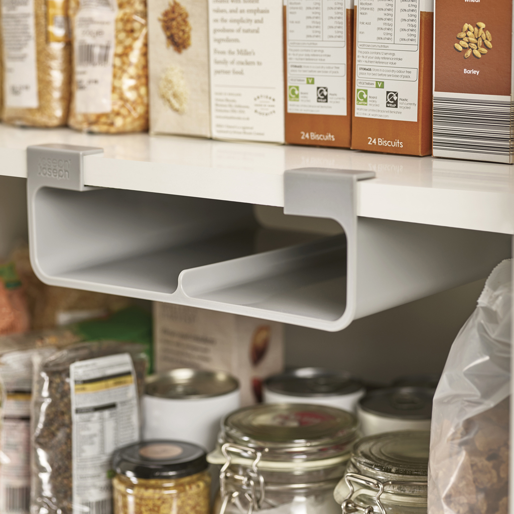 Un estante gris extraíble está instalado debajo de un estante blanco. Debajo hay frascos, latas y cajas de comida. Encima hay cajas de galletas.