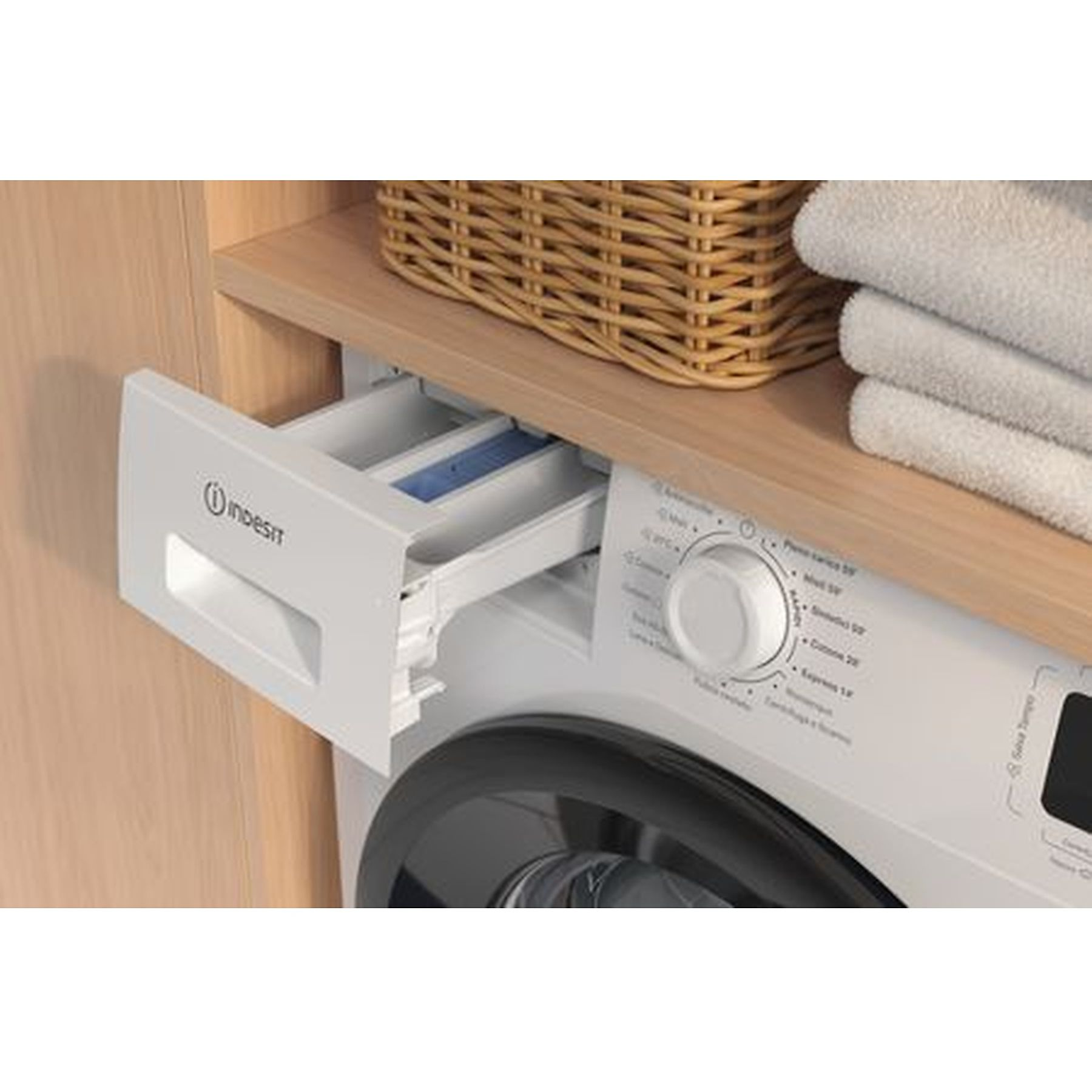 Una lavatrice Indesit bianca con cassetto detersivo aperto. Un cestino in vimini e asciugamani su una mensola di legno.