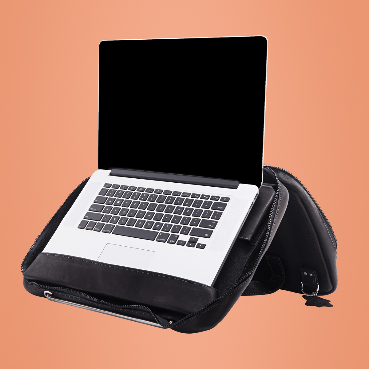 Un laptop è all'interno di una custodia in pelle nera, aperto e pronto all'uso. Lo sfondo è di colore arancione tenue.