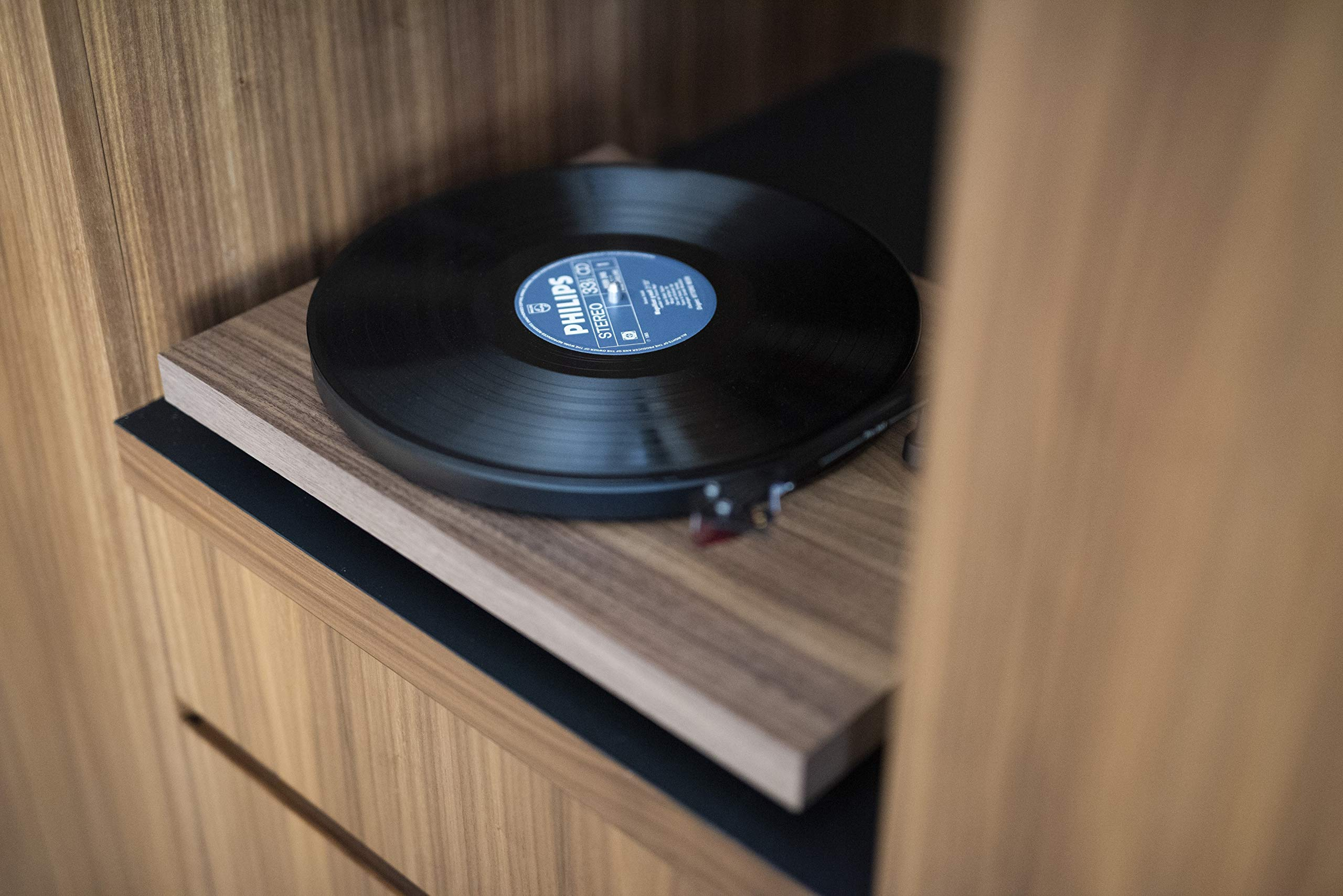 Een platenspeler met een zwarte vinylplaat staat op een houten plank. De achtergrond is een houten paneel.