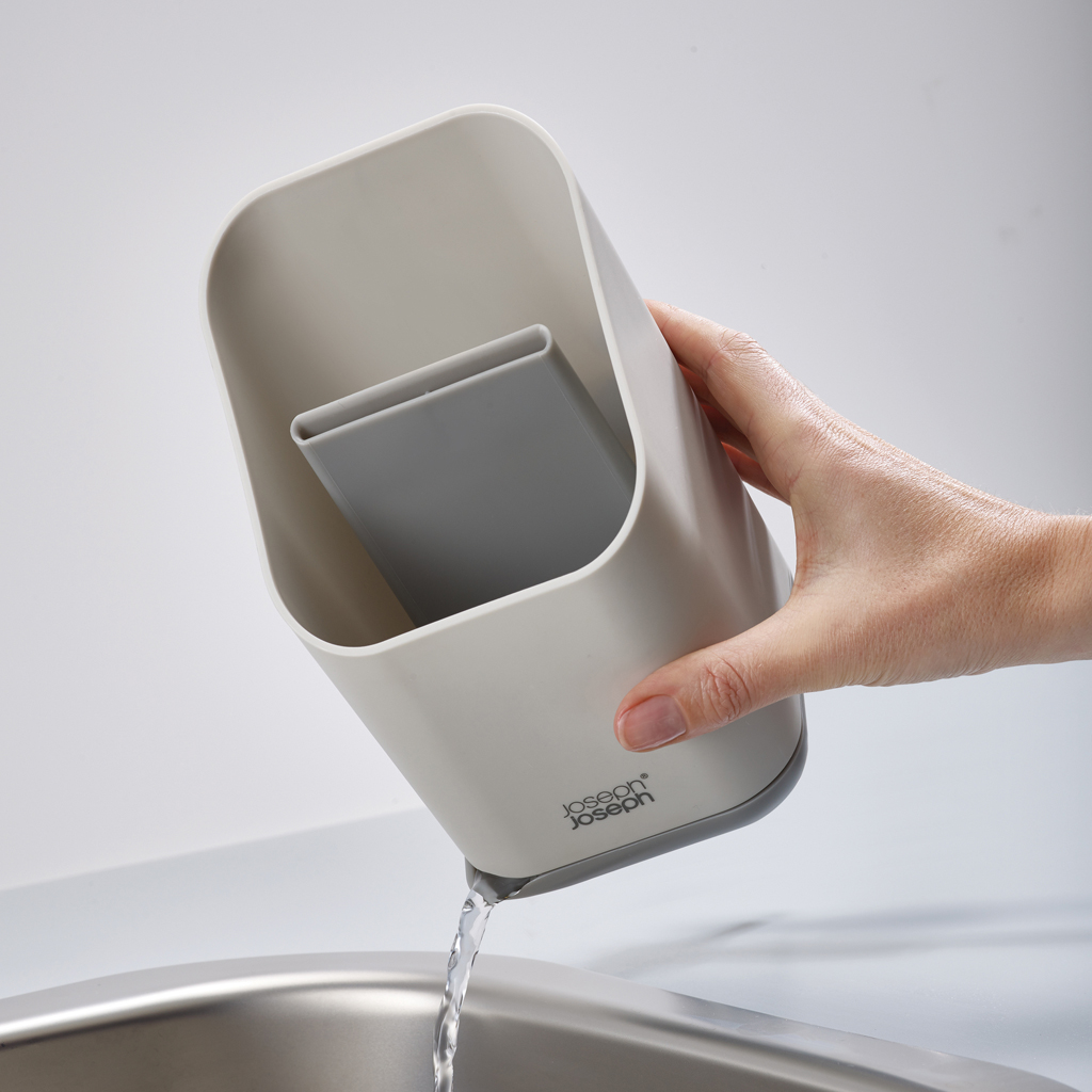 Una mano tiene un portautensili grigio e bianco, versando acqua in un lavandino in acciaio inossidabile. Il supporto ha un divisore grigio.