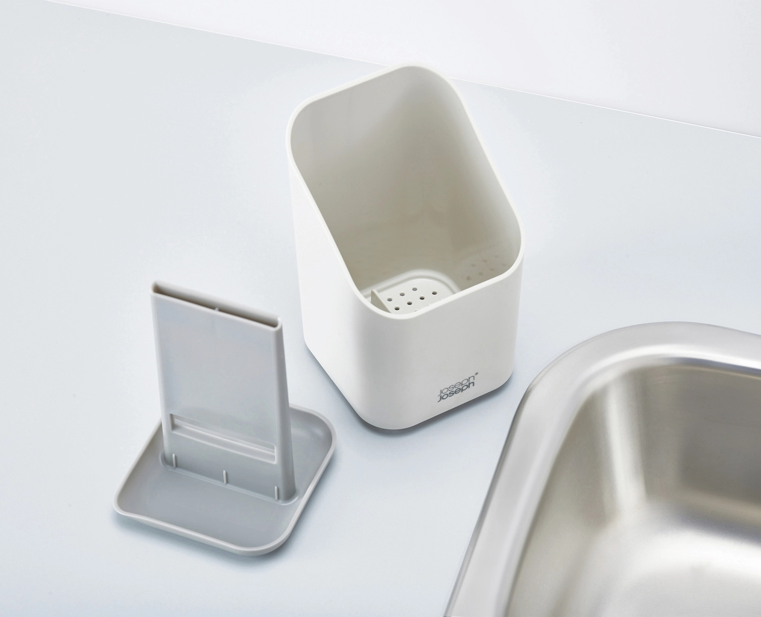 Un organizer bianco per lavello con un porta spugna grigio e un lavello in acciaio inox. L'organizer ha fori.