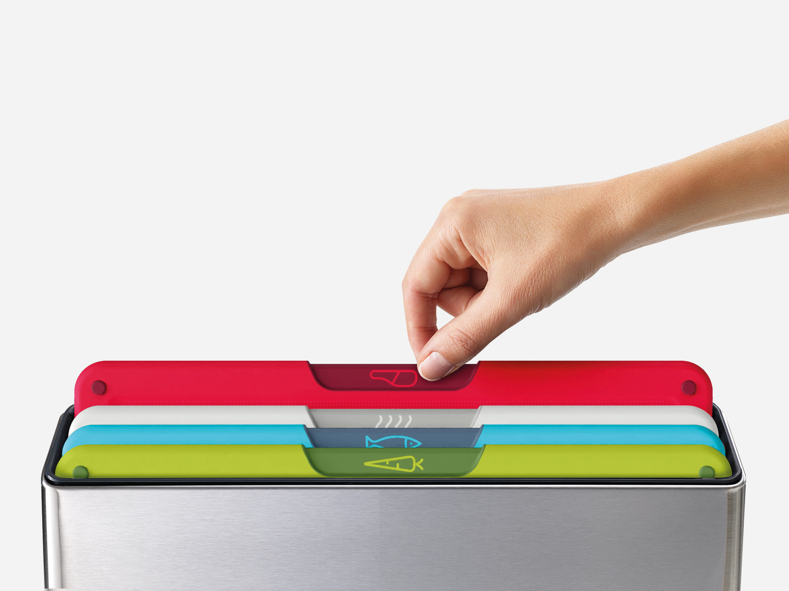 Mano sacando una tabla de cortar roja de una pila. Tablas rojas, blancas, azules y verdes, con iconos de comida. Base de acero inoxidable.
