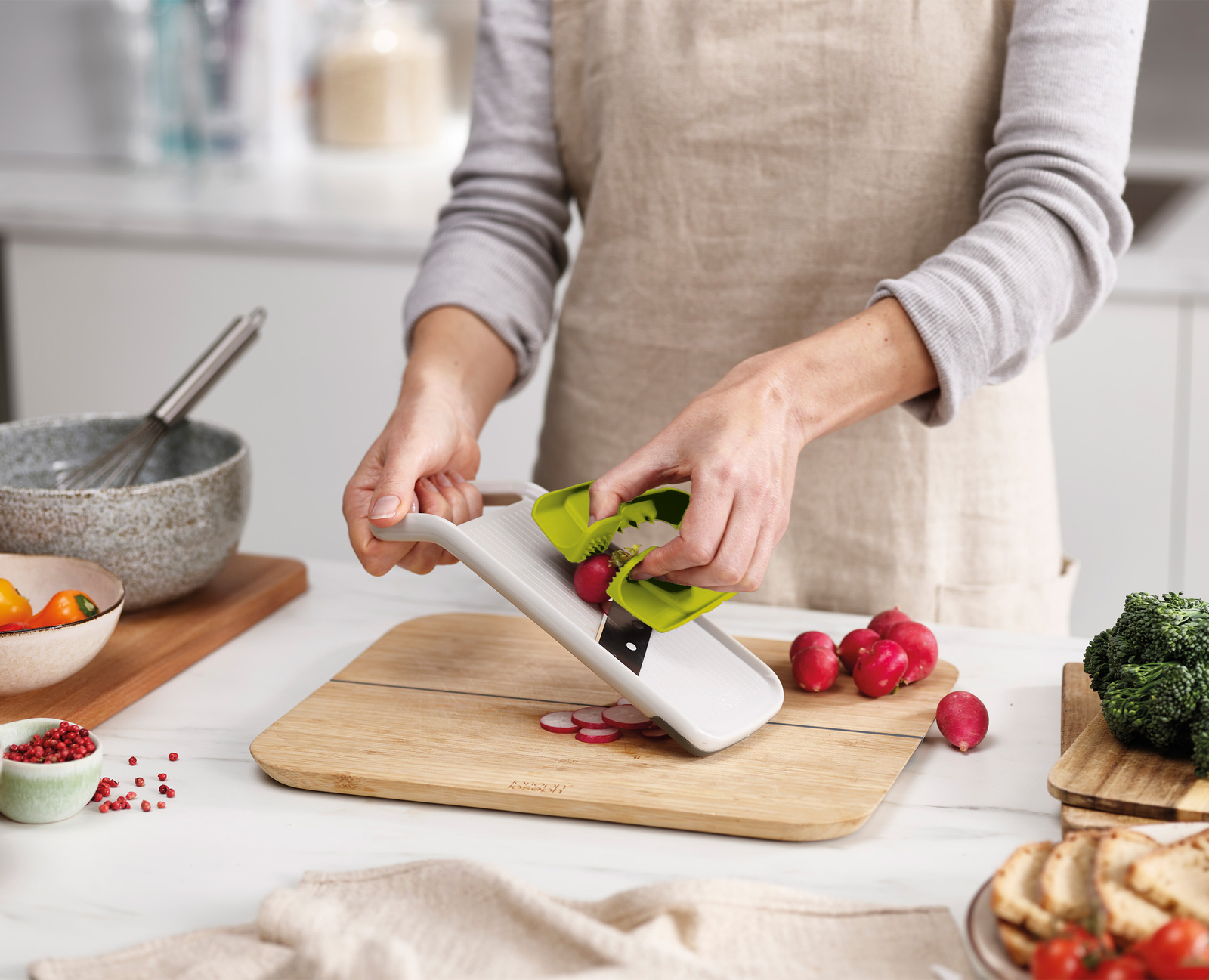 Una persona affetta i ravanelli con una mandolina su un tagliere di legno. Sono presenti altre verdure e ciotole.