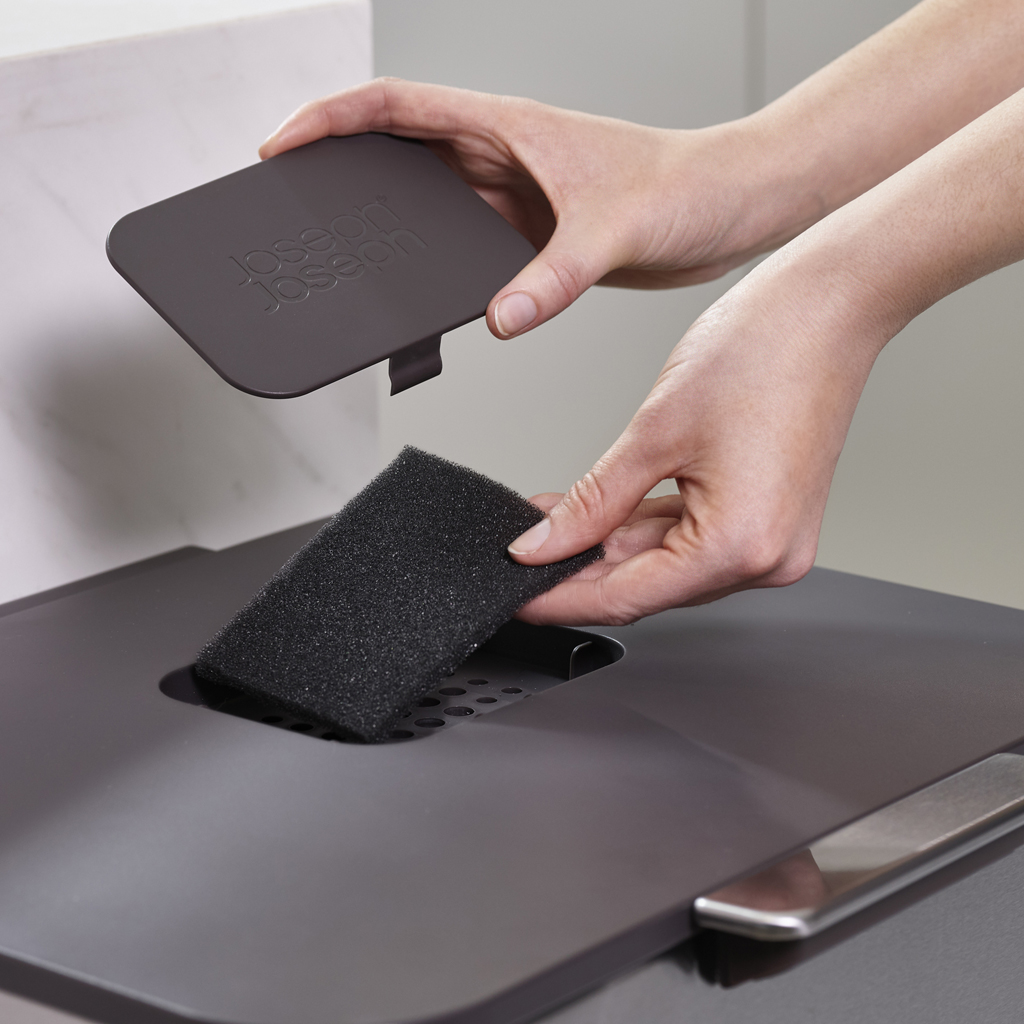 Mani che tengono un coperchio grigio e un filtro in spugna nero. Il coperchio è sopra il filtro e una superficie grigio scuro sotto.
