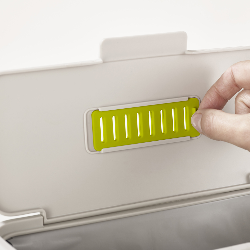Una mano inserta una pieza verde ranurada en un recipiente blanco. El recipiente tiene una tapa con bisagras. El fondo está borroso.