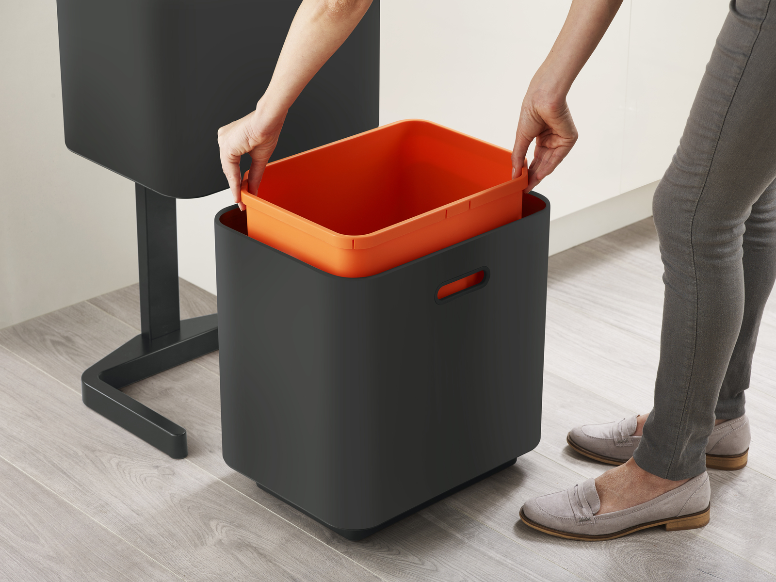 Manos colocando un cubo naranja en un cubo negro. Se ven pantalones y zapatos grises. Otro cubo negro en el fondo.