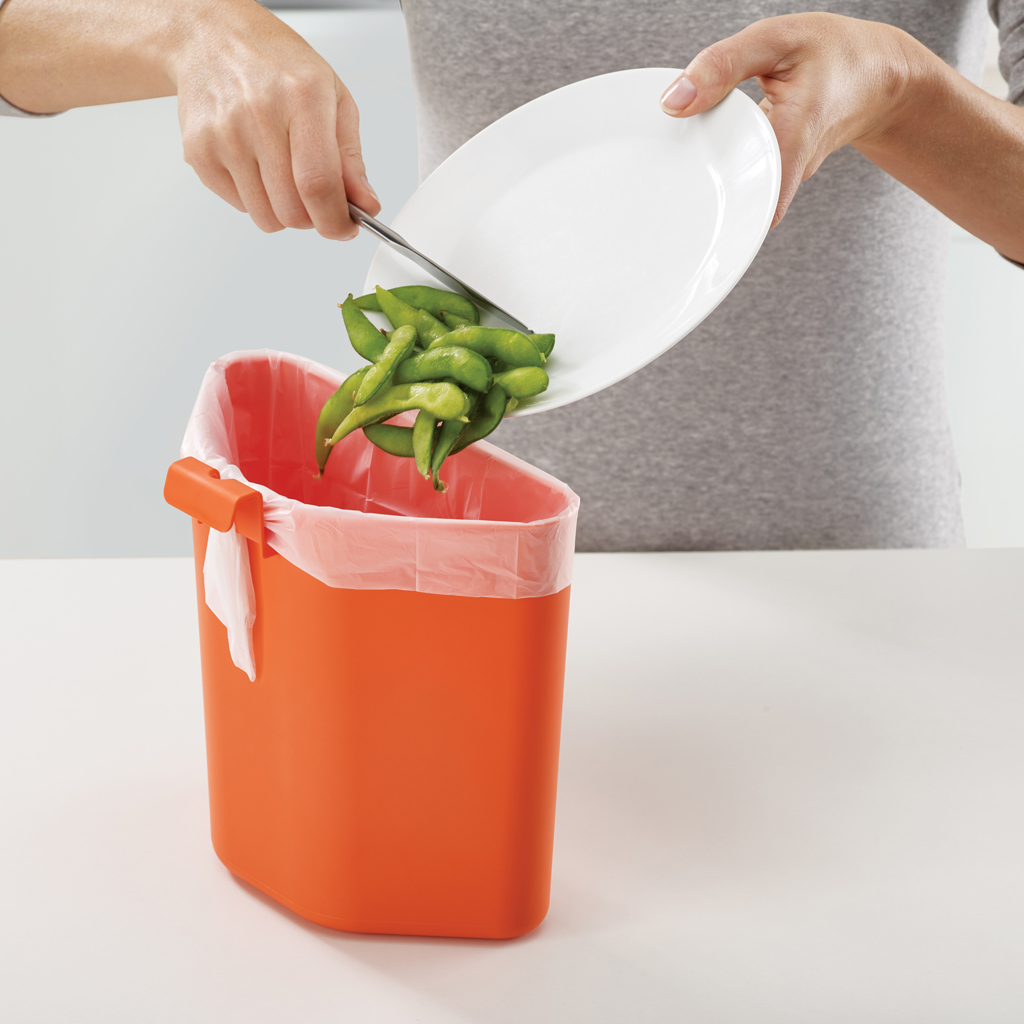 Una persona getta edamame da un piatto bianco in un cestino arancione. Il cestino ha un rivestimento bianco.