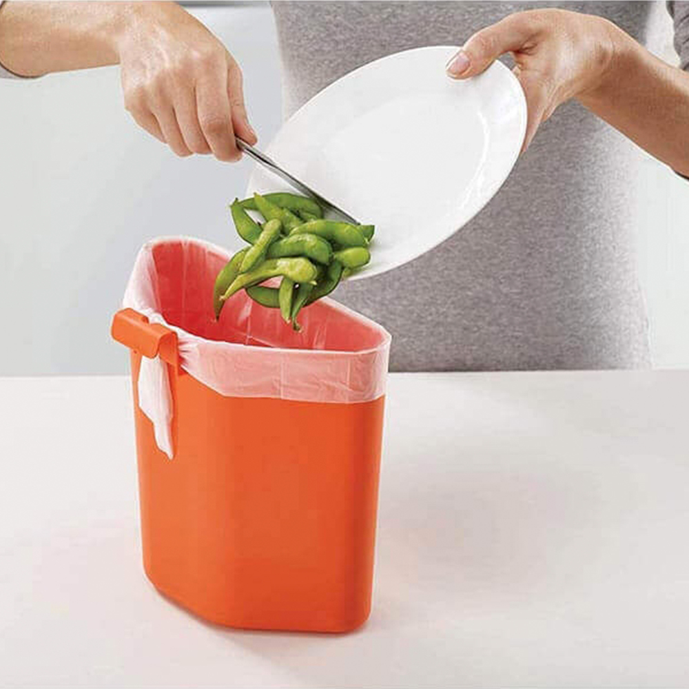 Una persona sta gettando edamame da un piatto bianco in un cestino arancione con fodera bianca.