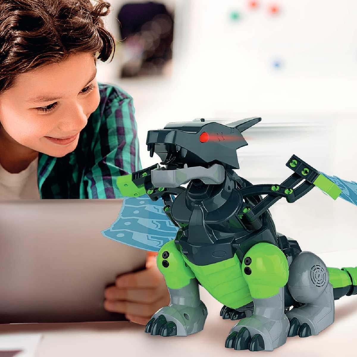 Un niño mira un dinosaurio robot verde y negro. Tiene alas azules. El niño sostiene una tableta. El fondo está borroso.