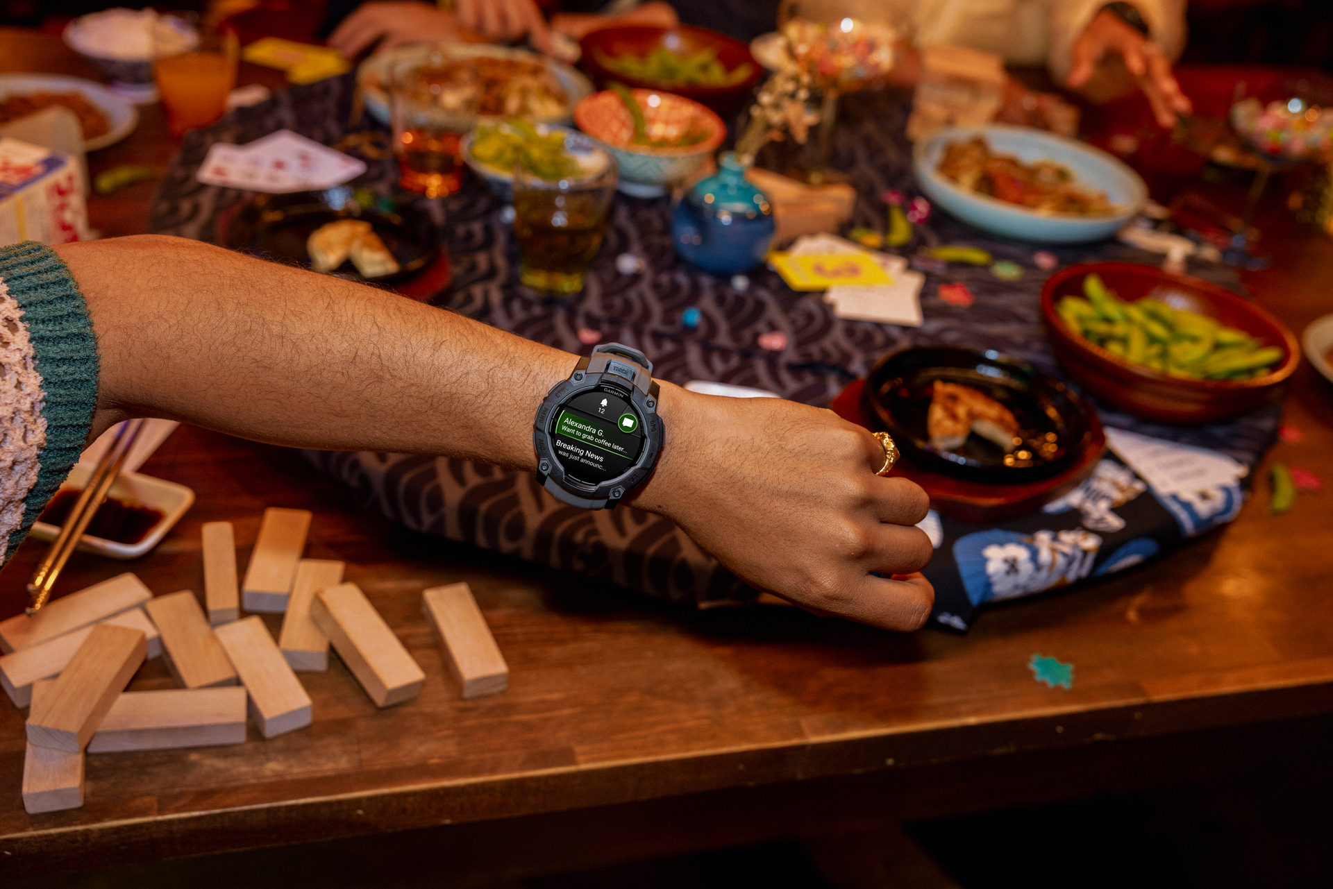 Een arm met een smartwatch, omringd door eten op een tafel. Het horloge toont een bericht. Houten blokken op de voorgrond.