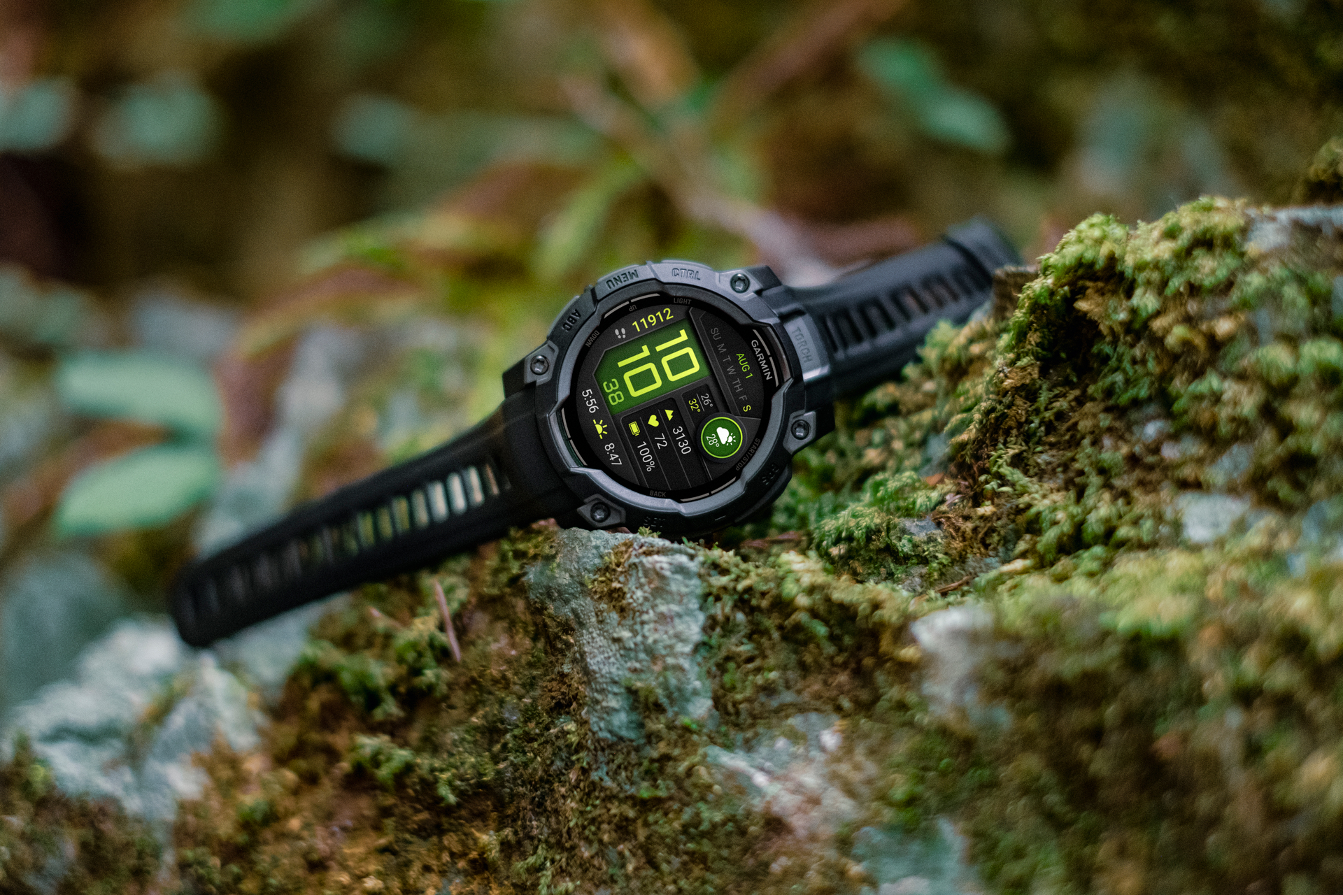 Eine schwarze Garmin-Uhr zeigt Zeit und Daten auf einem moosigen Felsen an. Der Hintergrund zeigt verschwommenes grünes Laub.