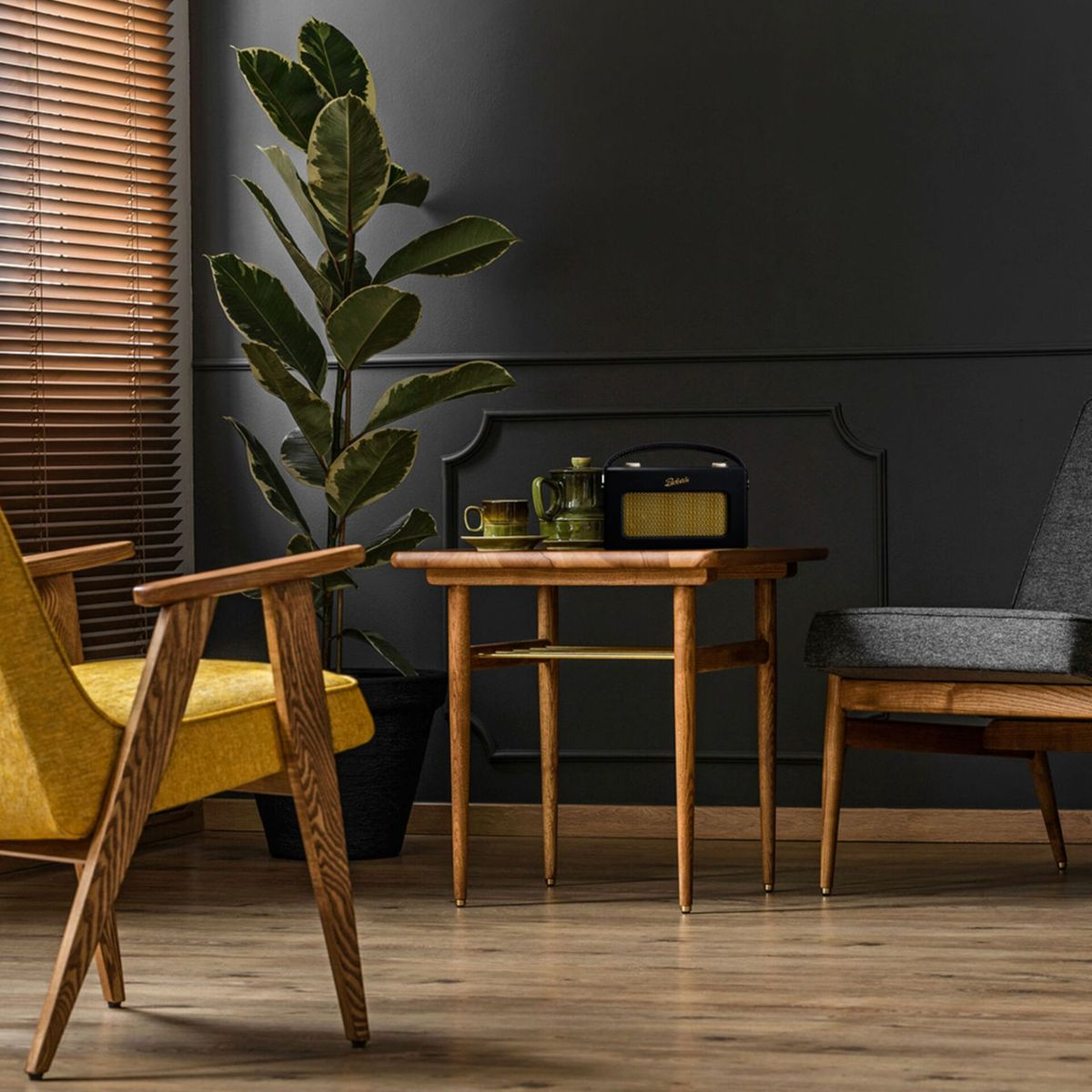 Pokój z żółtym fotelem, drewnianym stolikiem z radiem i zestawem do herbaty, wysoką rośliną i szarym fotelem.