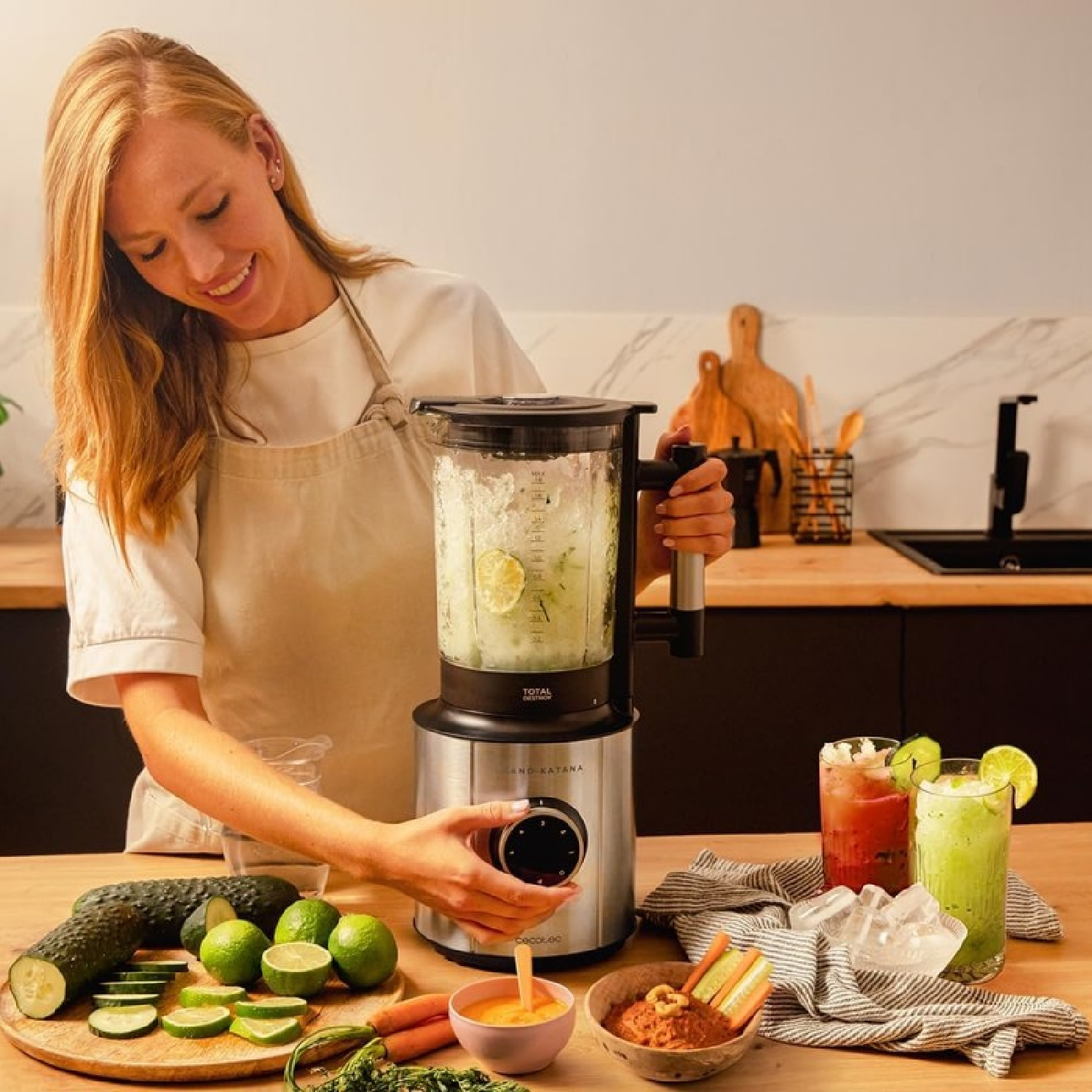 Kobieta robi smoothie blenderem. Składniki to ogórki, limonki i marchewki. Widoczne są dwie szklanki koktajli.