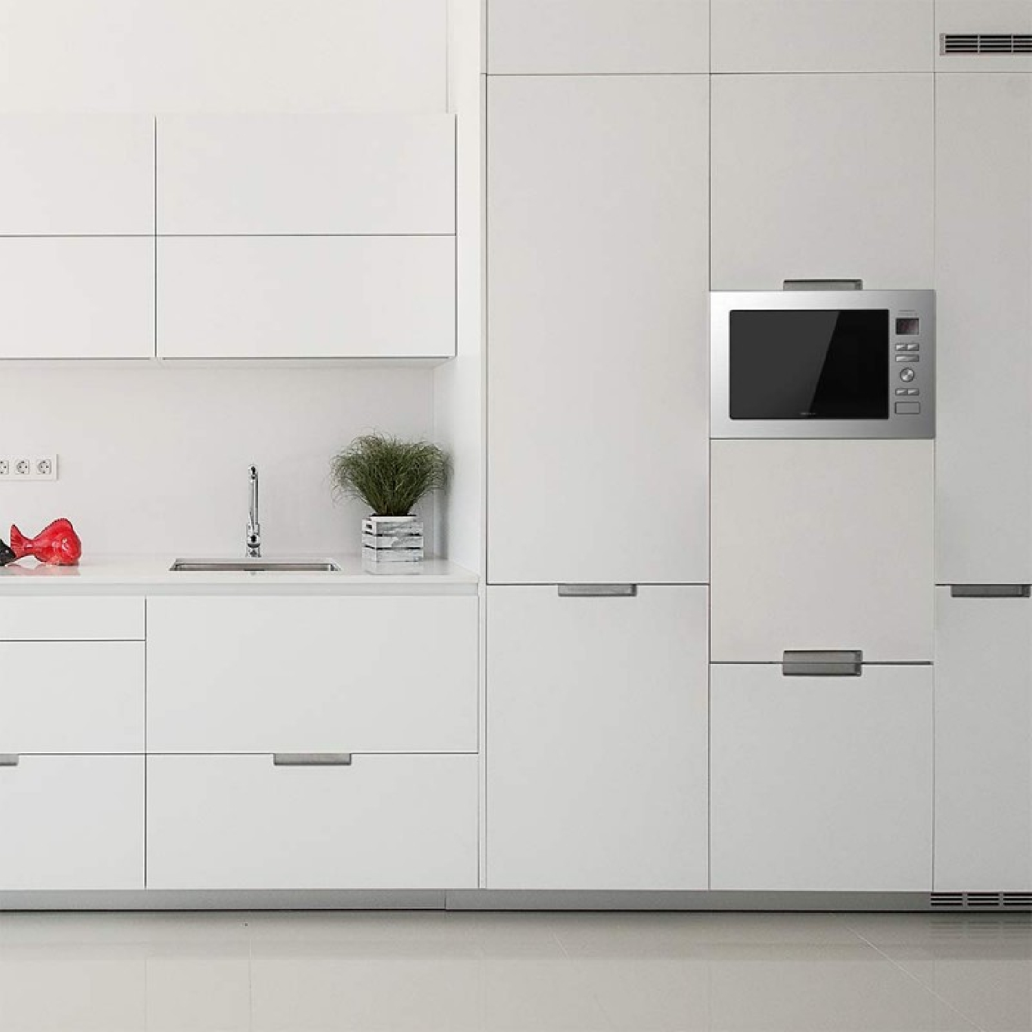 Nowoczesna biała kuchnia z szafkami, kuchenką mikrofalową, zlewem i czerwoną ozdobną rybą na blacie. Obecna jest również roślina.