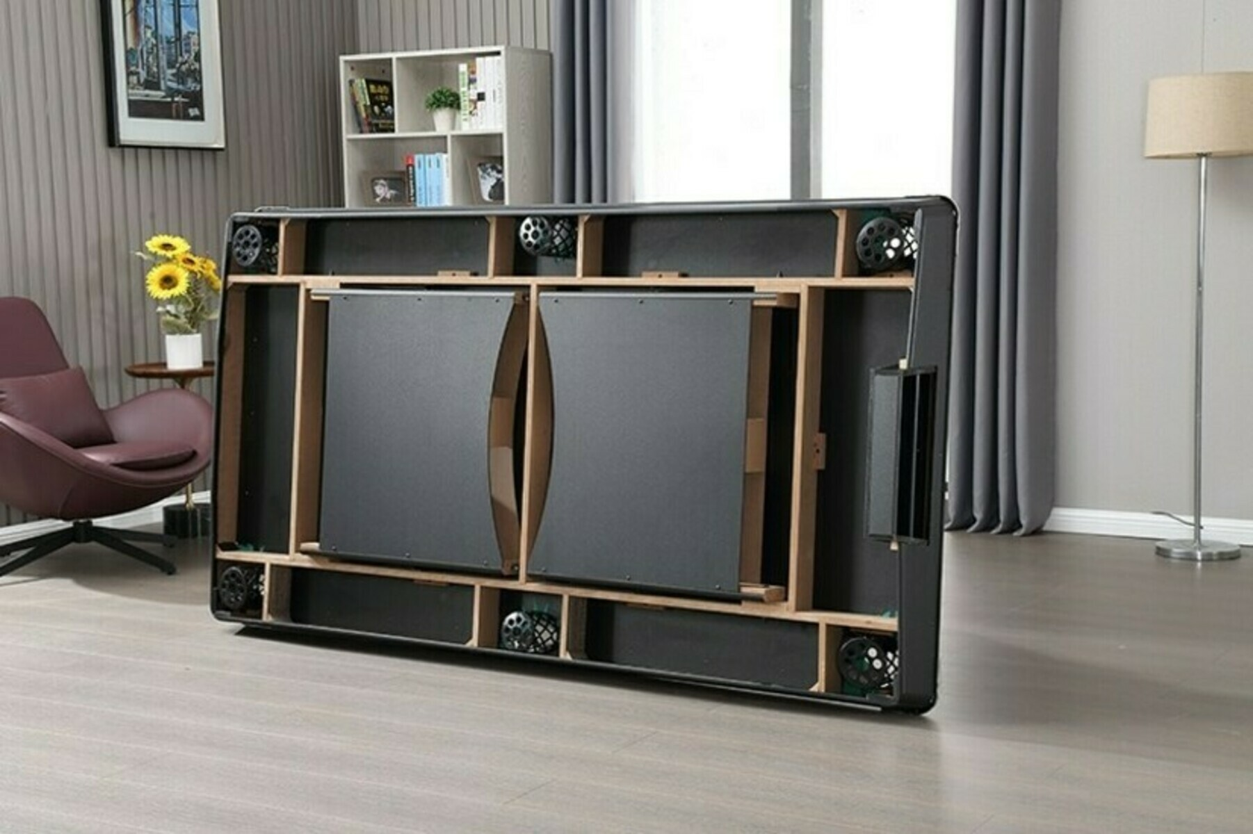 Een grote, zwarte opgevouwen structuur met luidsprekers. Een stoel, tafel en plank staan op de achtergrond.