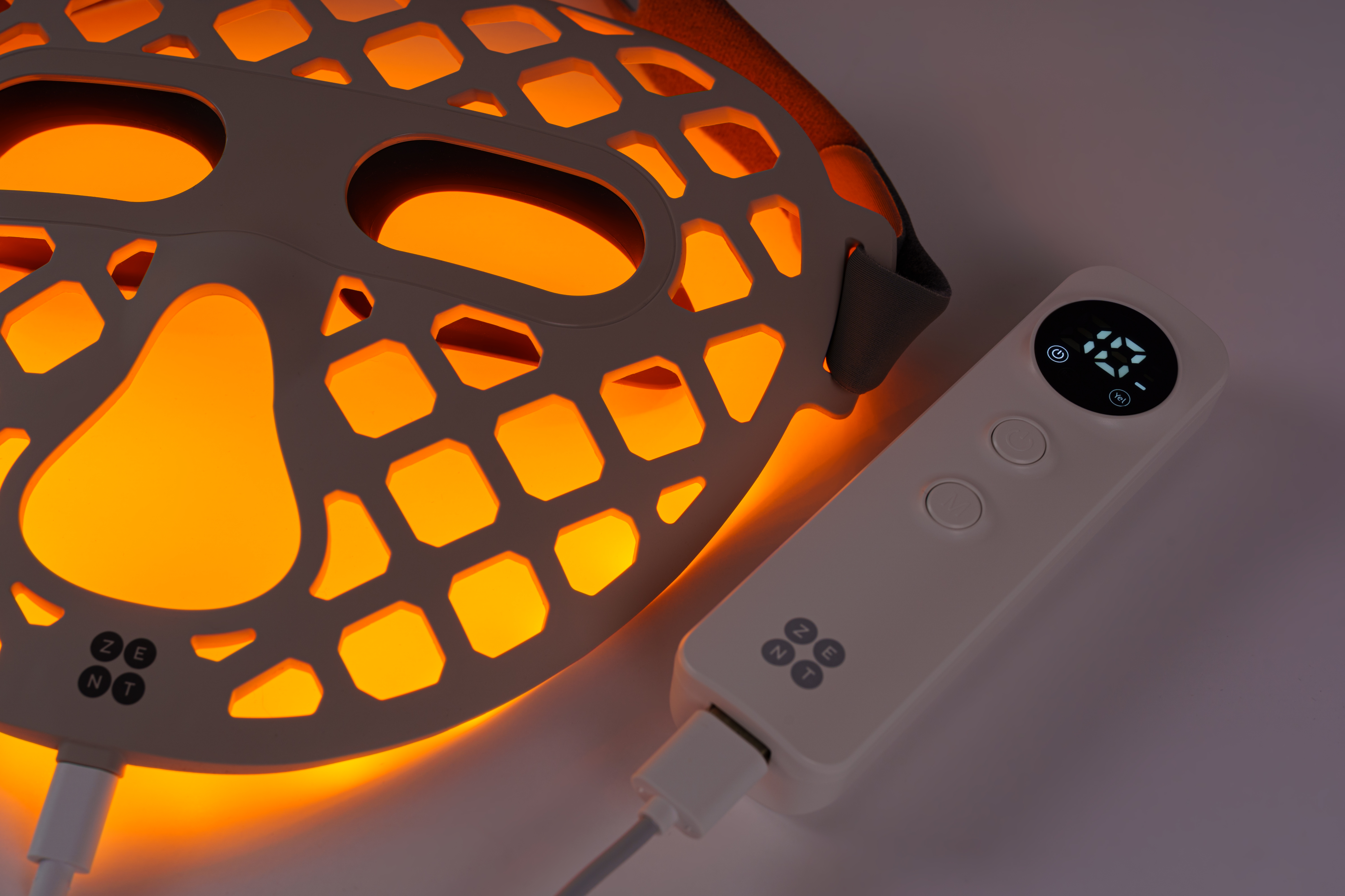 Świecąca maska na twarz z pilotem. Maska jest beżowa z pomarańczowym światłem w środku. Pilot jest biały.