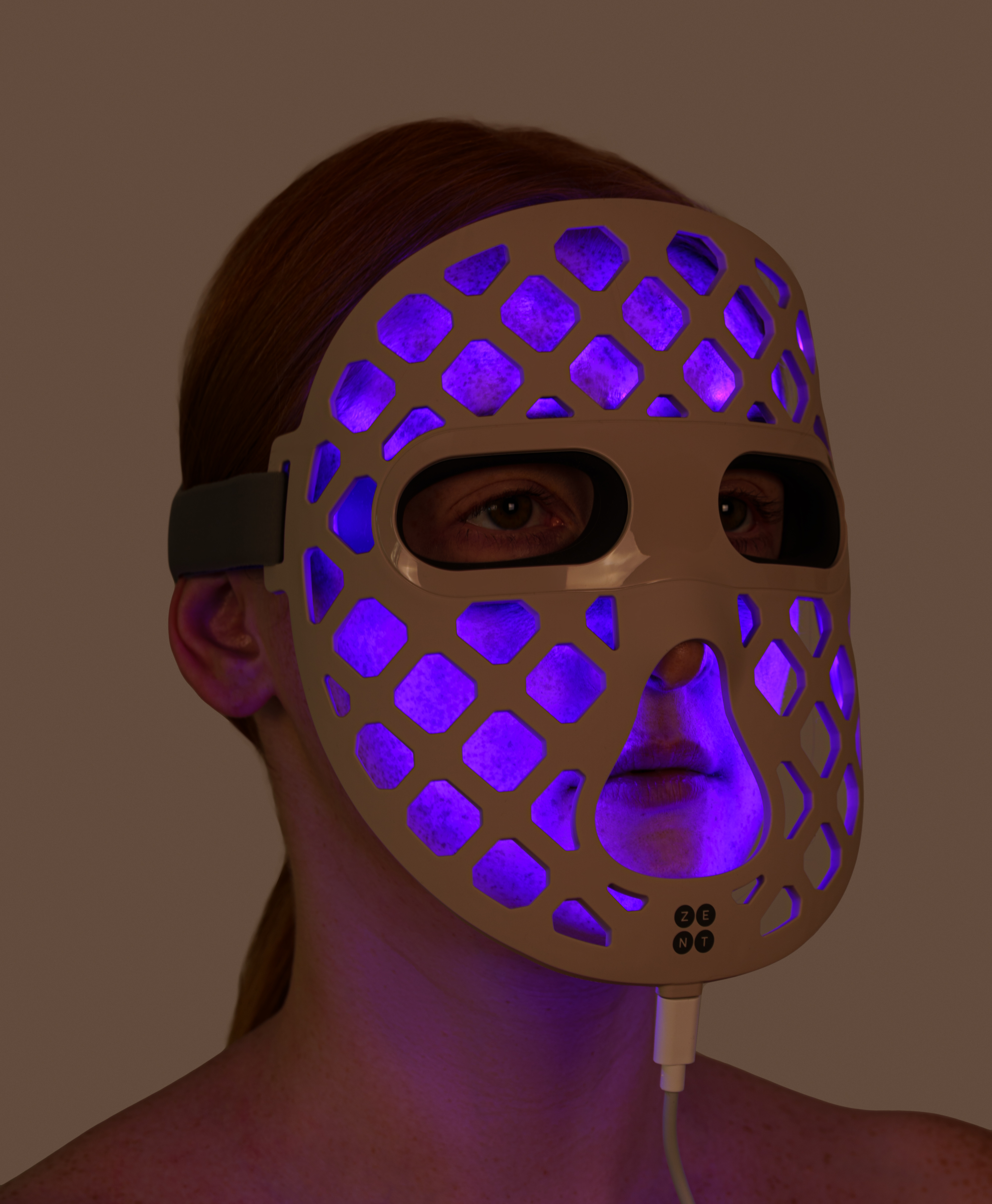 Osoba nosząca maskę na twarz z jasno fioletowymi światłami. Maska ma wzór kratki z otworami.