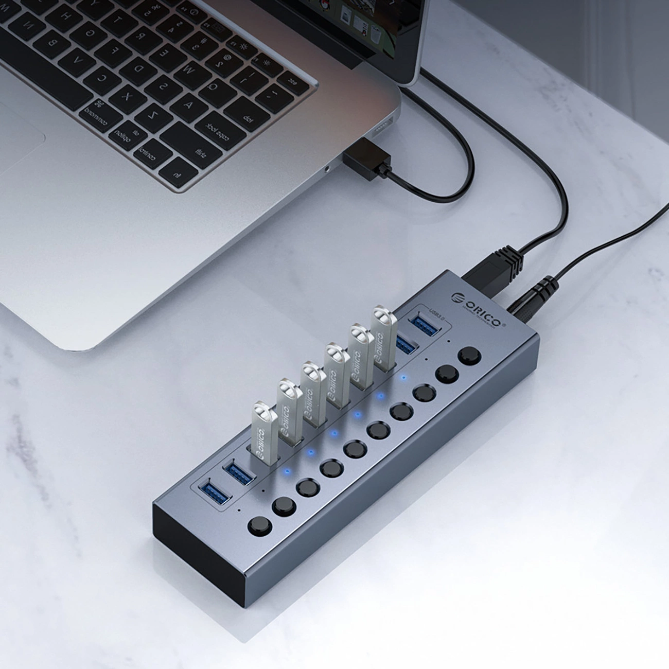 Laptop podłączony do koncentratora USB z wieloma dyskami USB. Hub jest szary, a laptop srebrny.