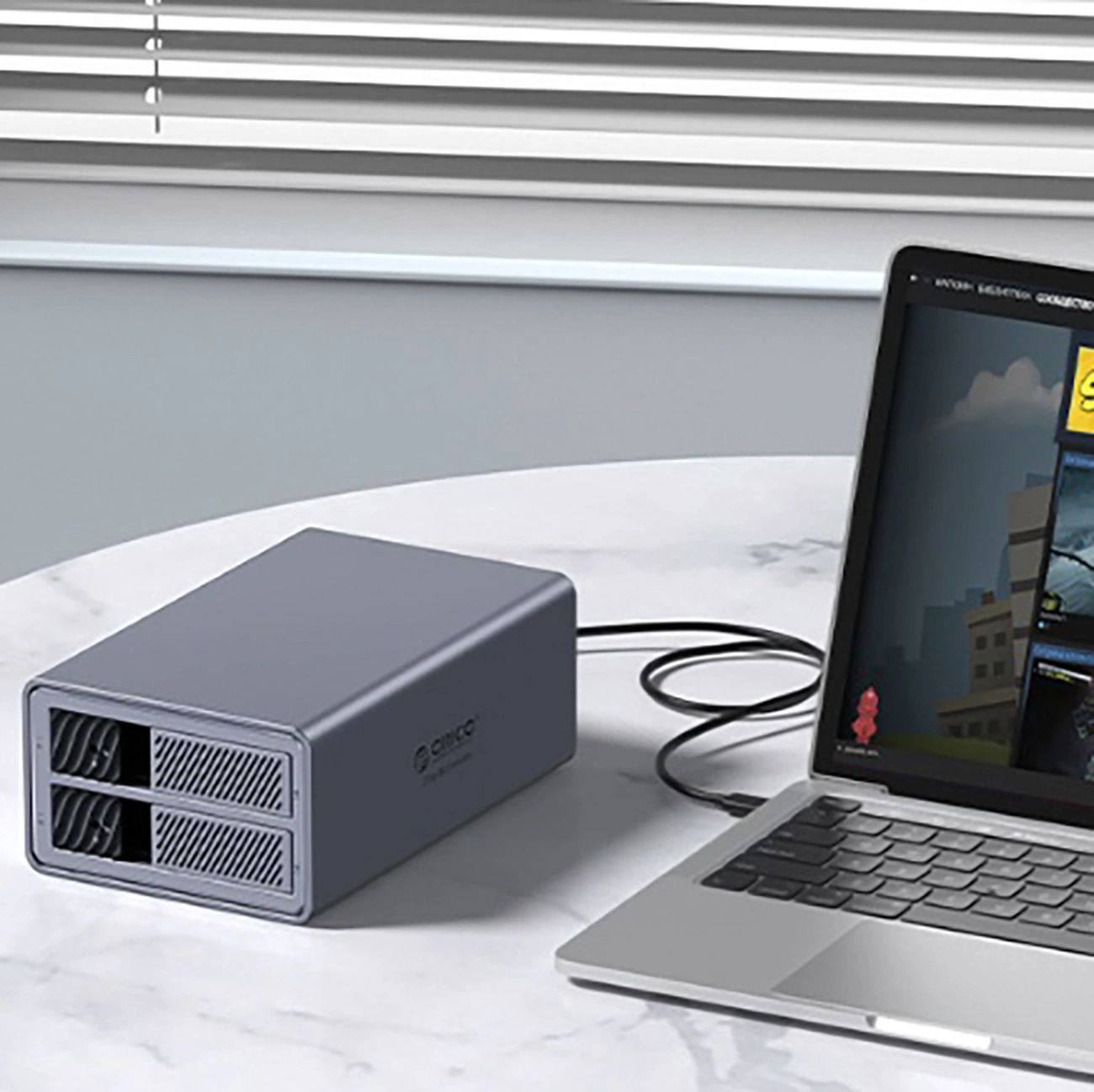 Szary zewnętrzny dysk twardy obok laptopa. Ekran laptopa wyświetla zawartość. Urządzenia znajdują się na okrągłym stole.