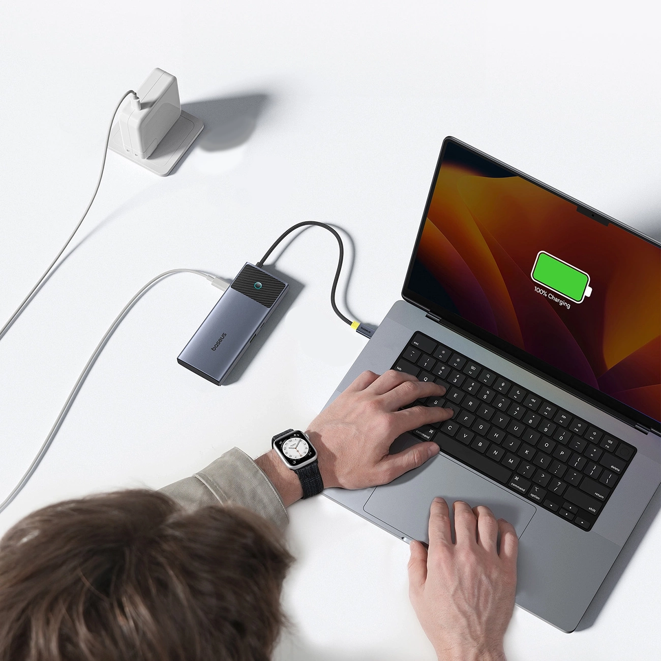 Ein Laptop wird aufgeladen, verbunden mit einer Powerbank. Eine Person tippt auf der Tastatur. Eine Uhr ist am Handgelenk.