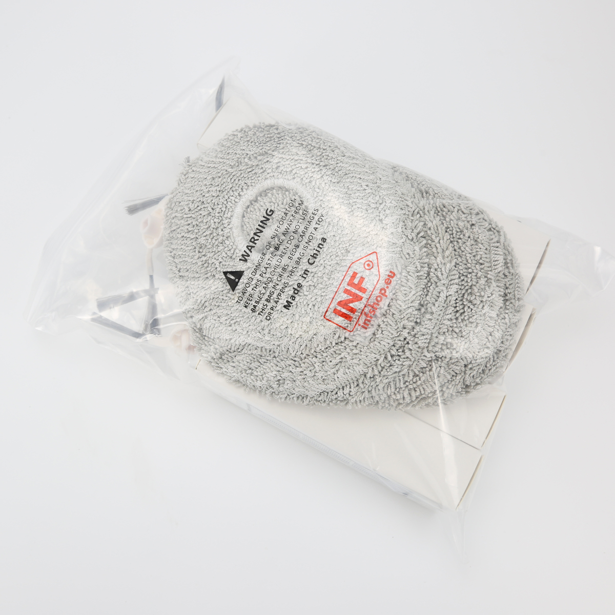 Un tampone per la pulizia grigio e accessori sono all'interno di un sacchetto di plastica trasparente. La borsa contiene anche una scatola di cartone bianca. Lo sfondo è bianco.