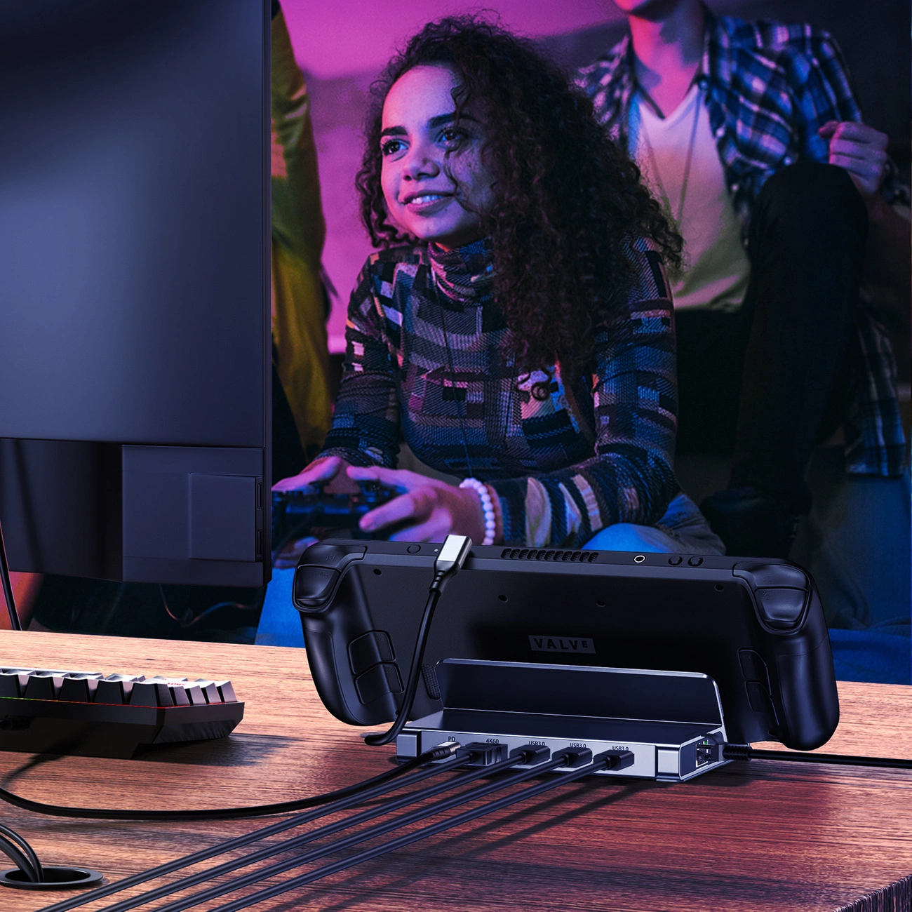 Eine Frau spielt mit einem Controller, Steam Deck in einer Dockingstation, Monitor und Tastatur sind sichtbar.