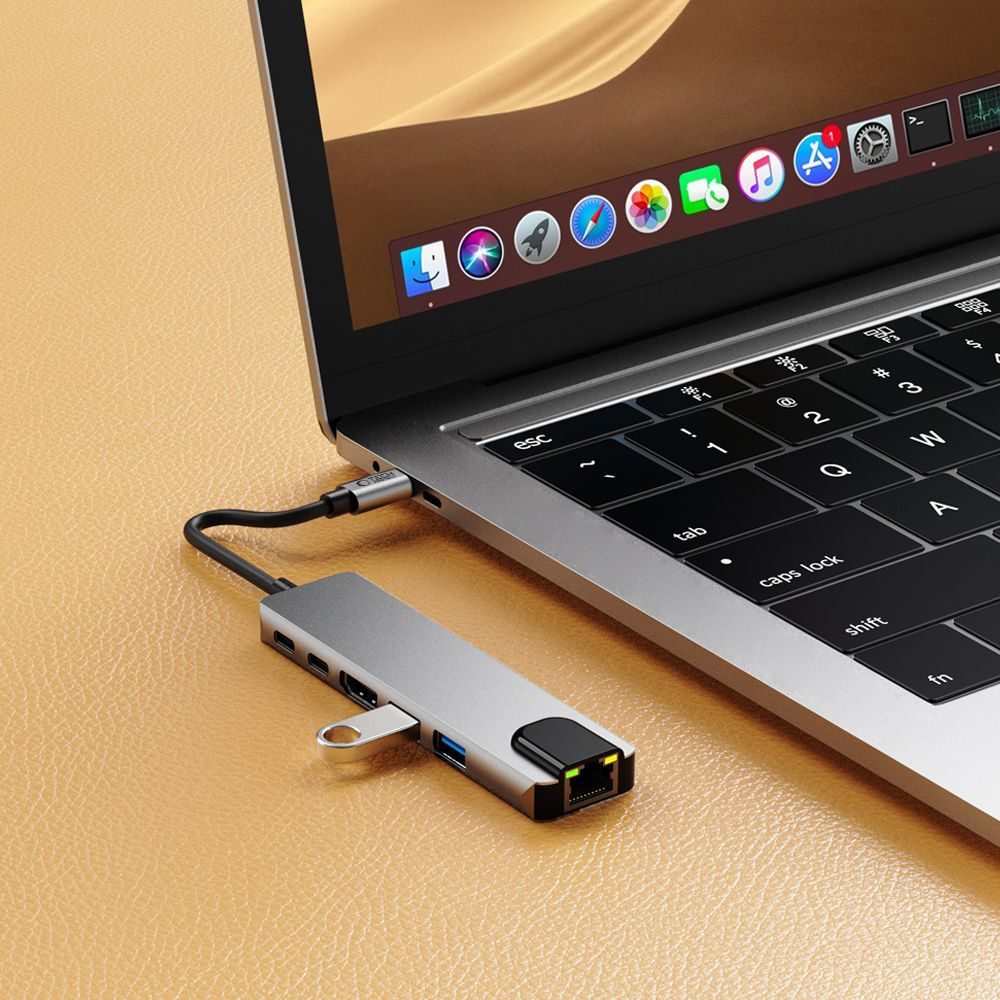 Een laptop met een zilveren hub aangesloten. De laptop is open en toont het toetsenbord en scherm. De achtergrond is een bruin oppervlak.