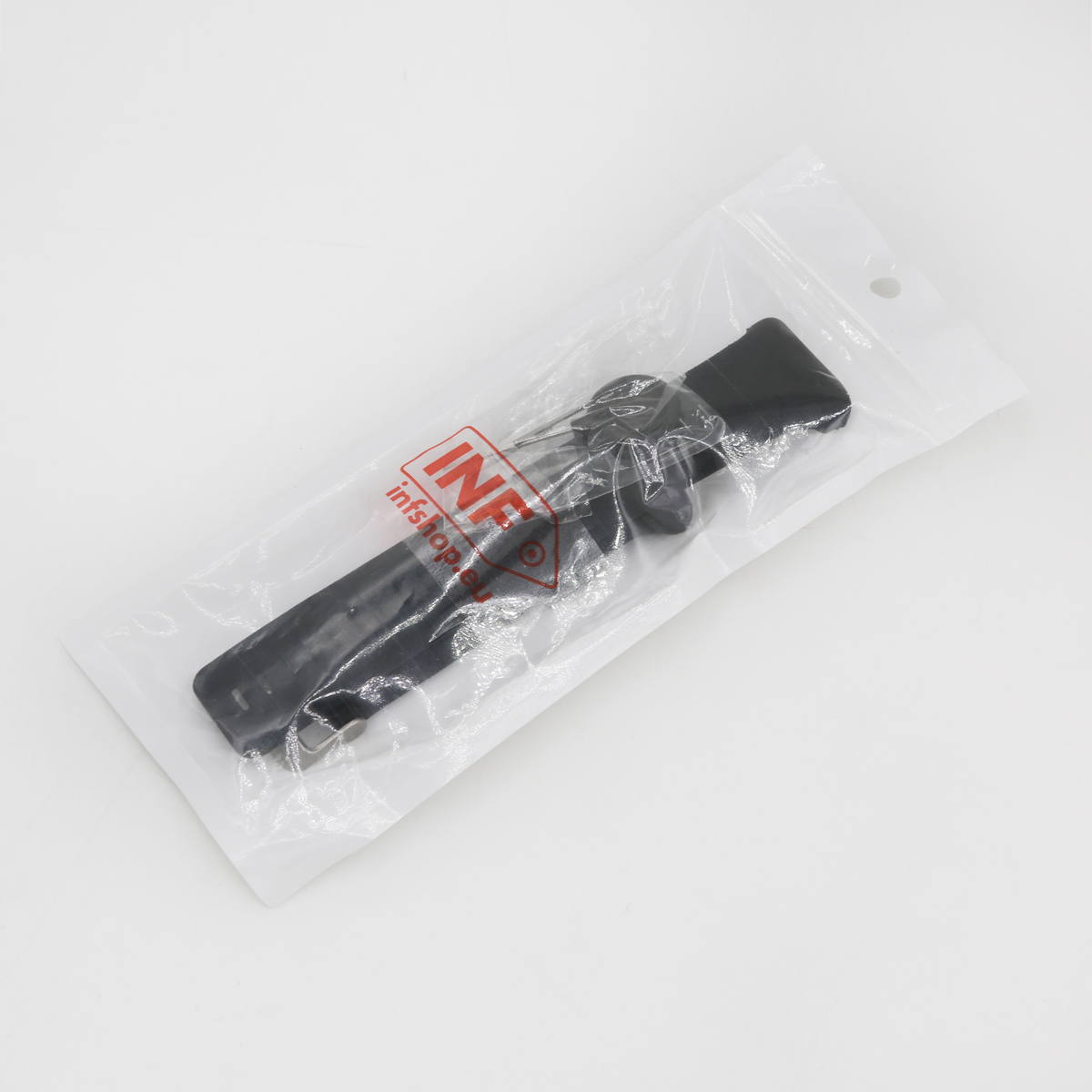 Ein schwarzer Gegenstand in einer durchsichtigen Plastiktüte mit einem rot-weißen Logo. Die Tüte liegt auf einer weißen Oberfläche.