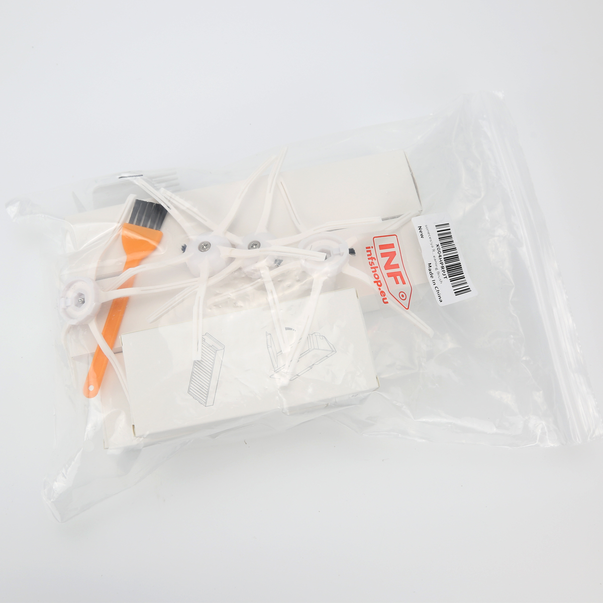 Opakowanie zawierające akcesoria do robota sprzątającego, w tym szczotki, małą pomarańczową szczoteczkę i białe pudełko, wszystko w przezroczystej torbie.