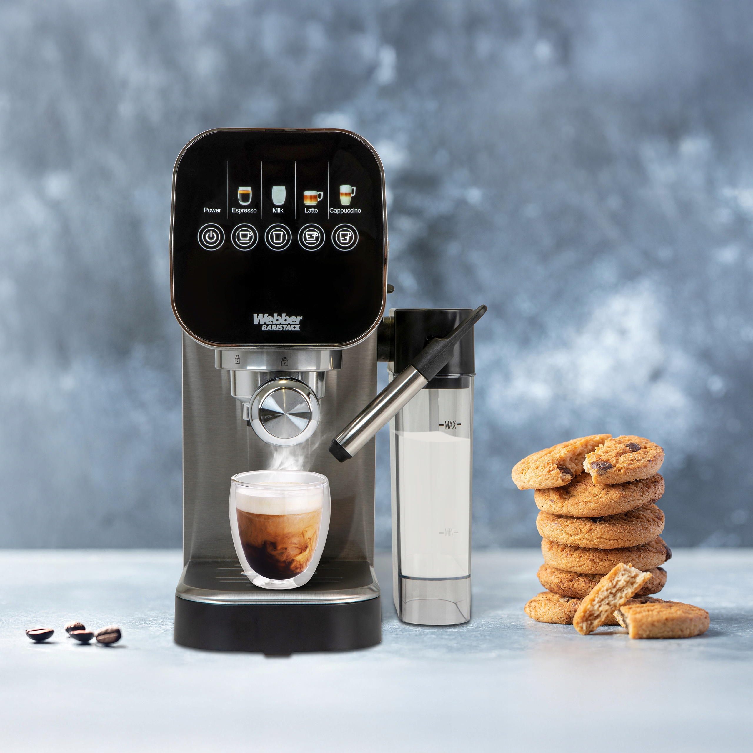 Ekspres do kawy ze szklanką kawy, spieniaczem do mleka, ciastkami i ziarnami kawy na szarej powierzchni.