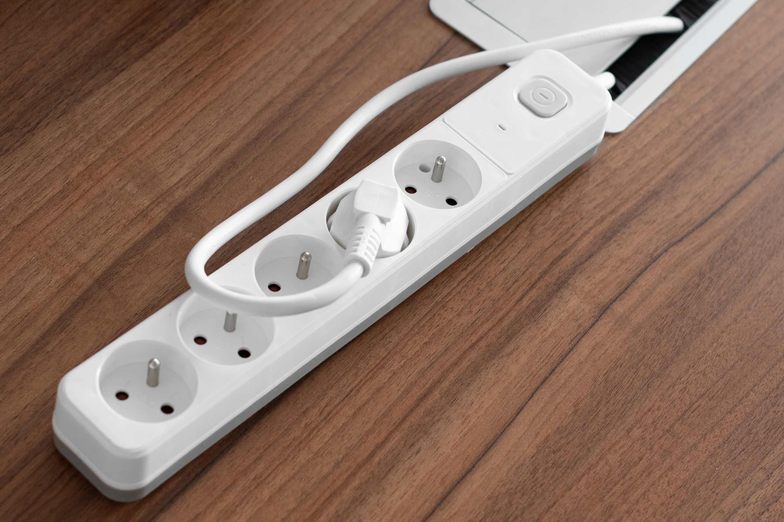 Biała listwa zasilająca z włożoną wtyczką na drewnianej powierzchni.