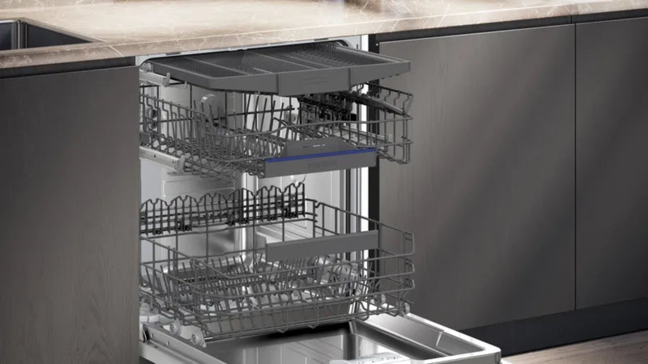 Otwarta zmywarka z dwoma koszami. Ciemnoszare kosze w szafce. Blat kuchenny widoczny w tle.