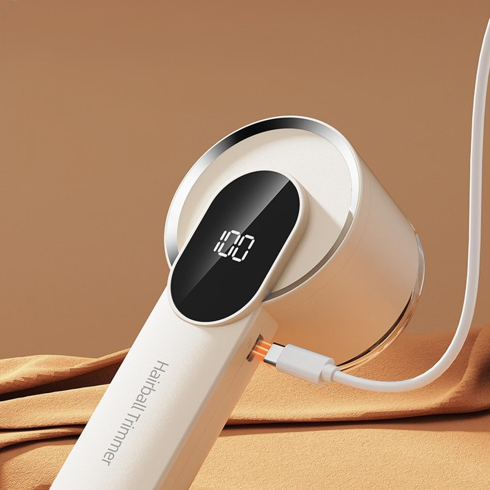 Ein weißer Fusselrasierer mit digitaler Anzeige, die 100 % Ladung anzeigt, USB-C-Kabel eingesteckt. Der Hintergrund ist braun.
