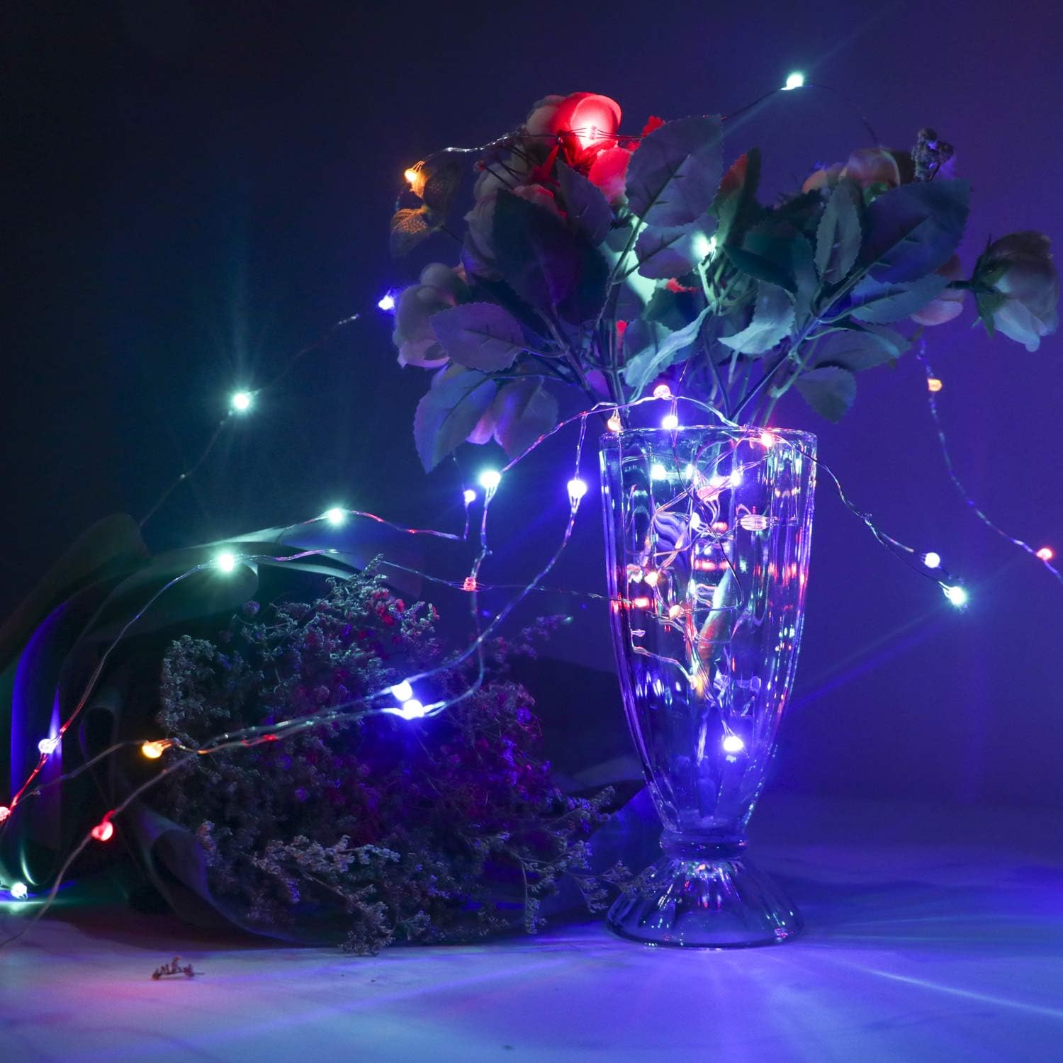 Eine Vase mit Blumen und Lichterketten. Die Lichter sind bunt und der Hintergrund ist dunkelblau und lila.