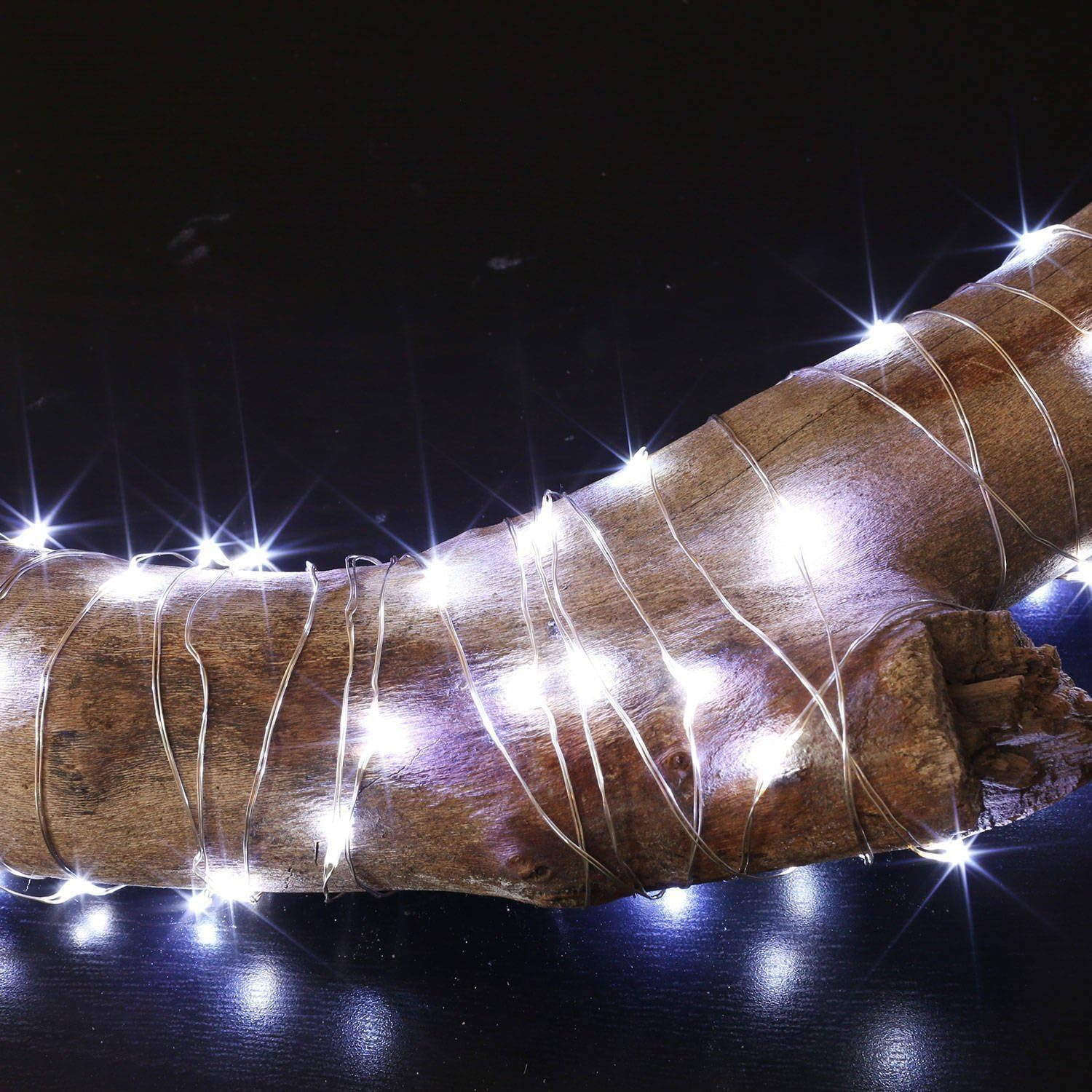 Nahaufnahme eines Holzstücks, das mit weißen Lichterketten verziert ist. Dunkler Hintergrund mit Lichtreflexen.