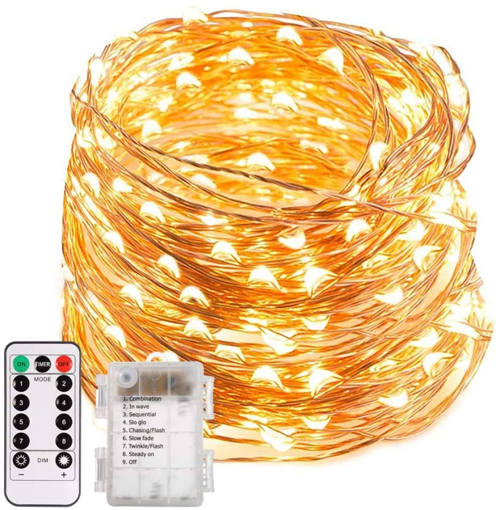 Nahaufnahme einer Schnur aus kleinen, warmweißen LED-Leuchten, die aufgerollt sind. Eine Fernbedienung und eine Batteriebox sind ebenfalls sichtbar.