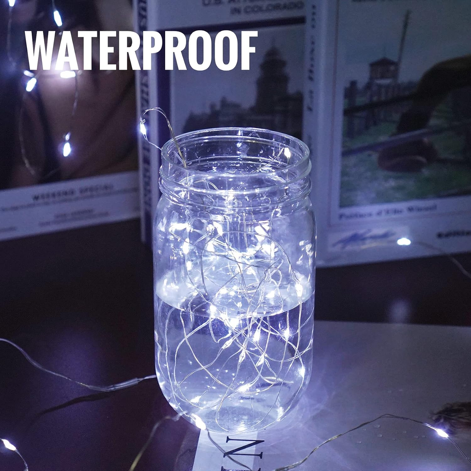 Ein Glas mit Wasser und Lichterketten. Das Wort WASSERDICHT steht oben. Bücher sind im Hintergrund.