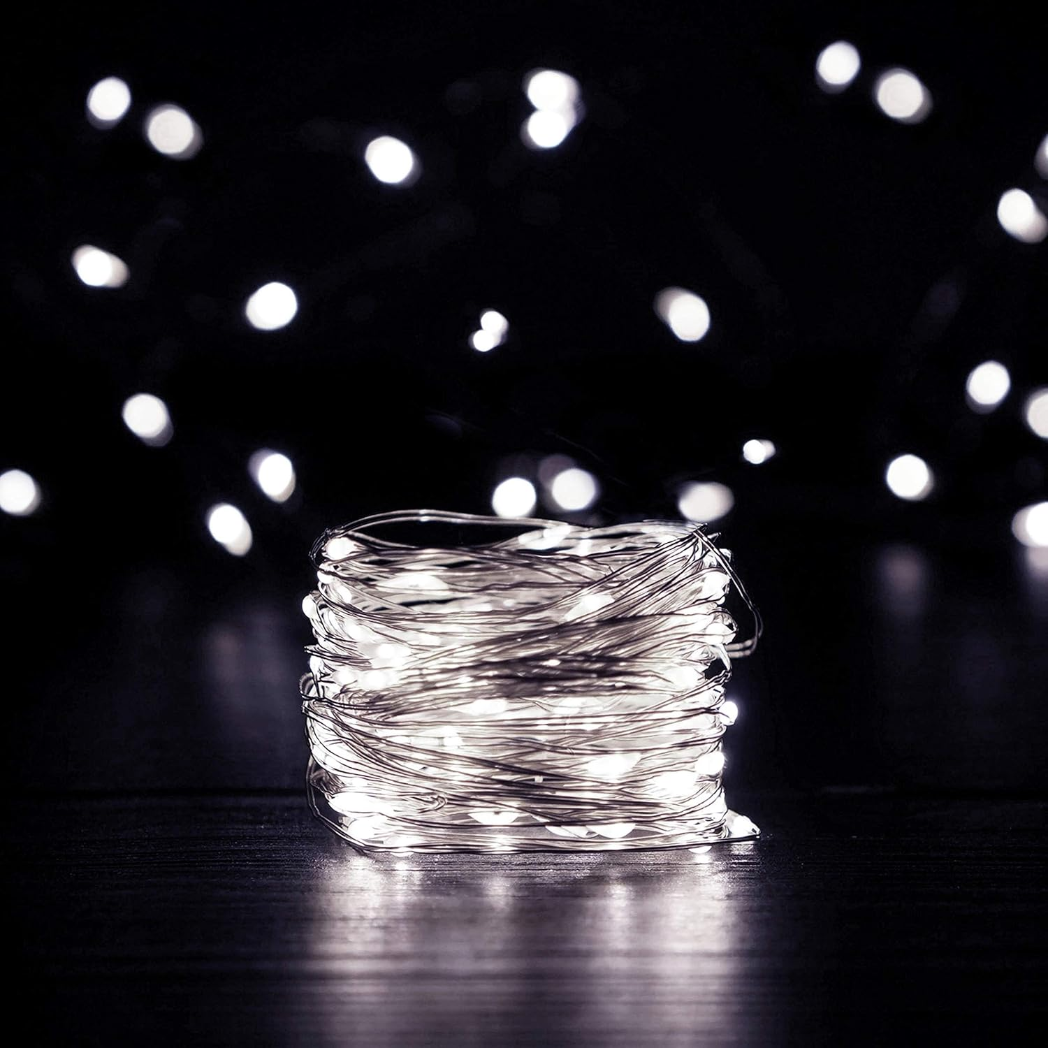 Ein Bündel silberner Drahtlichter auf dunkler Oberfläche. Unscharfe weiße Lichter im Hintergrund. Die Szene ist dunkel.