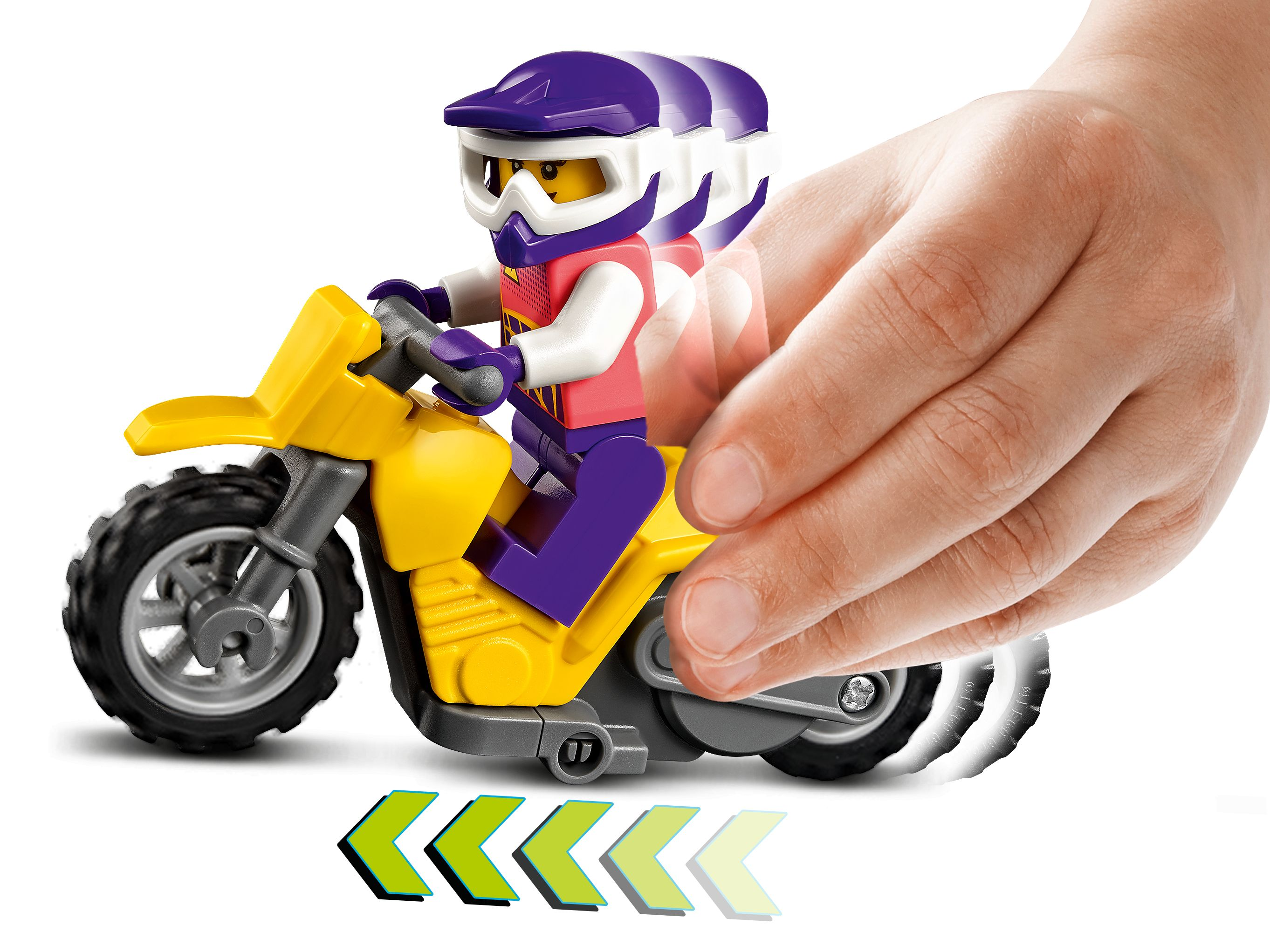 Ein gelbes Spielzeugmotorrad mit einem lila Helmfahrer wird von einer Hand geschoben. Bewegungslinien zeigen Bewegung an.