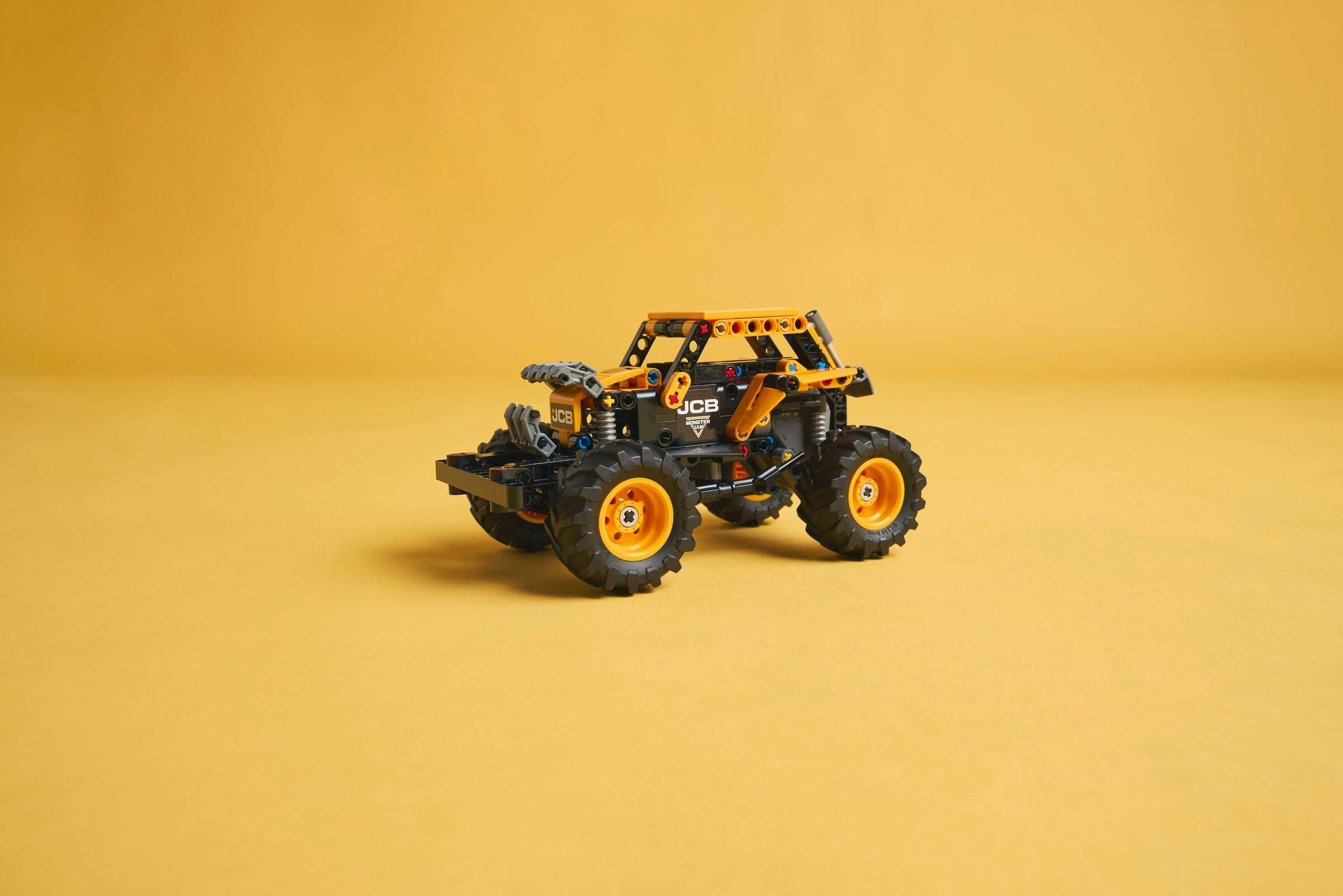 Ein gelb-schwarzes Spielzeug-Monstertruck mit großen Reifen steht auf gelbem Hintergrund.
